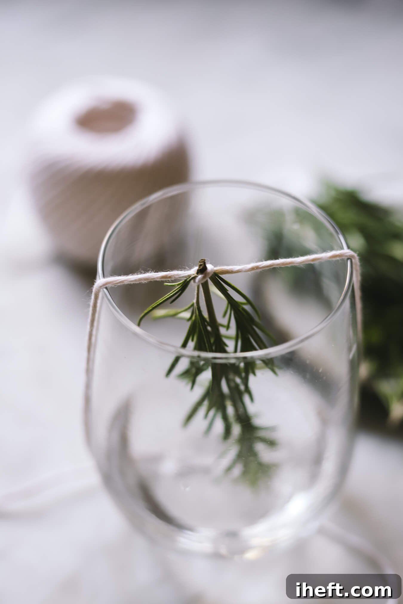 Twine wrapped around the top of a rosemary sprig and across the top of a stemless wine glass.