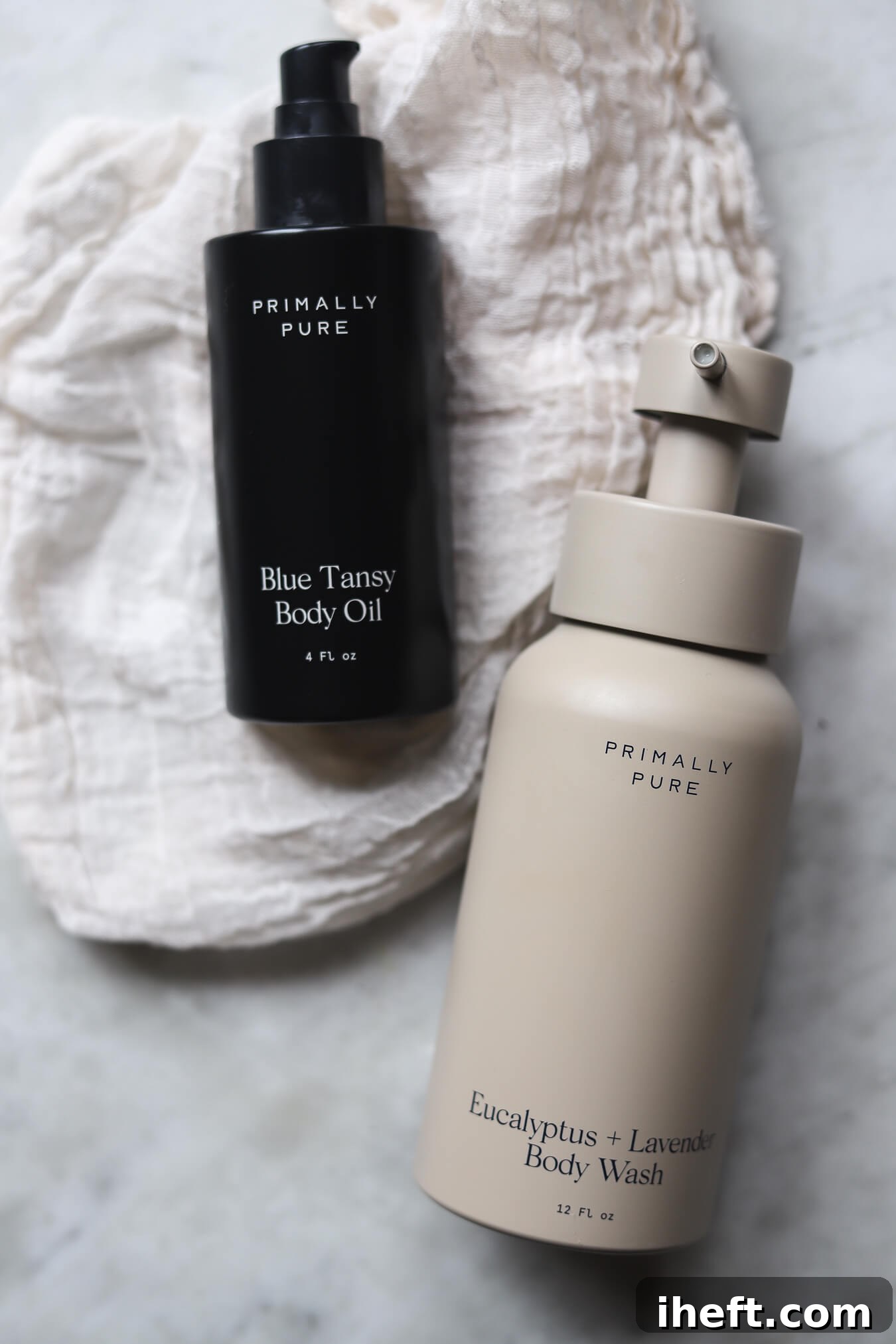 Primally Pure Blue Tansy Body Oil and Eucalyptus + Lavender Body Wash bottles on a marble counter, evoking a spa-like cleanliness and luxury.