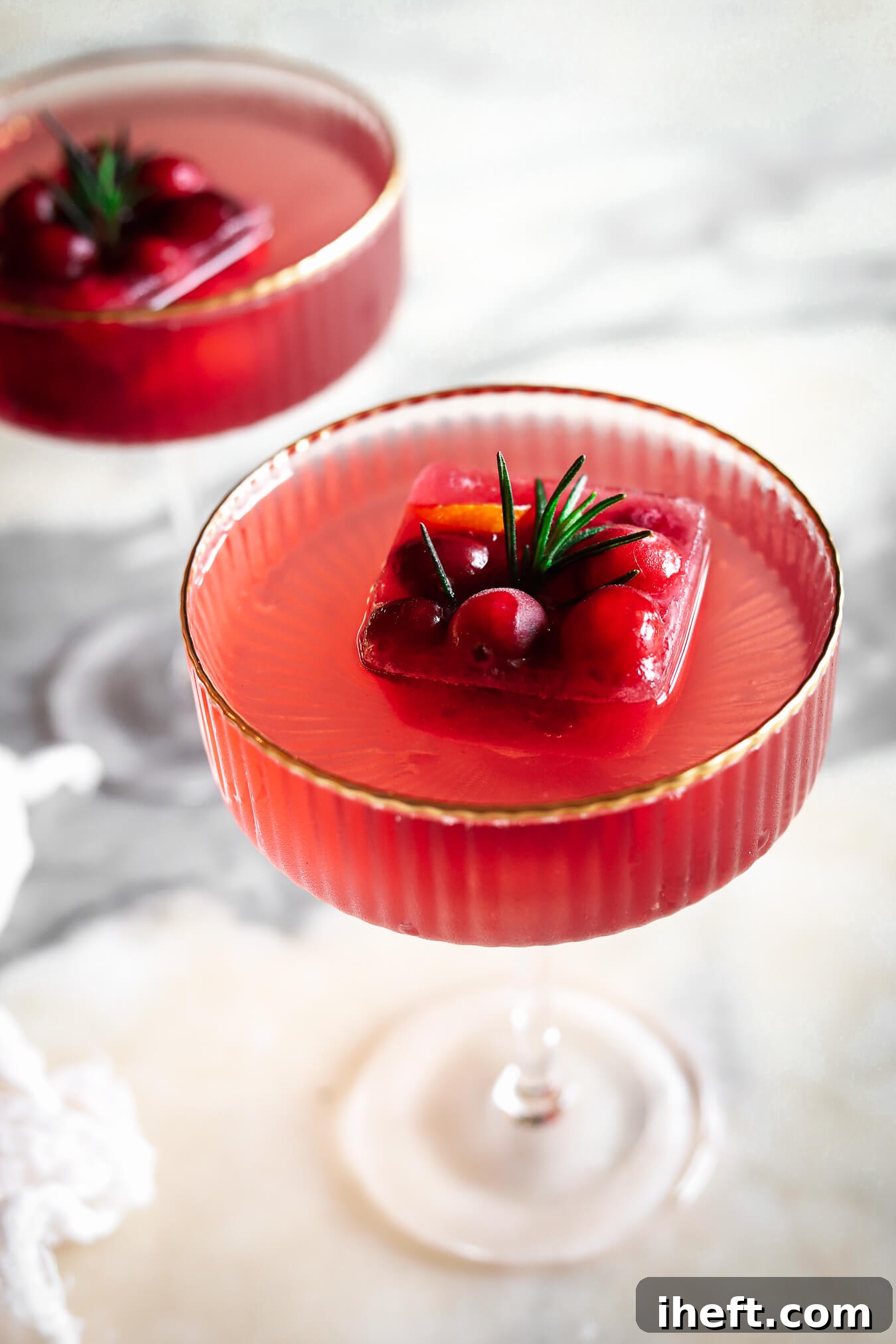 Two Christmas drinks with fancy cranberry ice cubes with fresh cranberries and rosemary. 