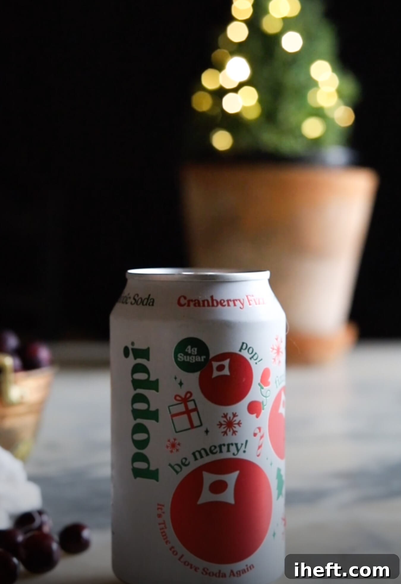 A can of poppi cranberry fizz prebiotic soda on a marble counter with a small potted Christmas tree in the background. 