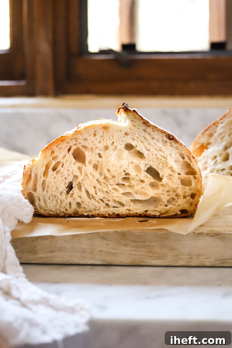 A woman sits at a marble table scoring an unbaked sourdough batard.