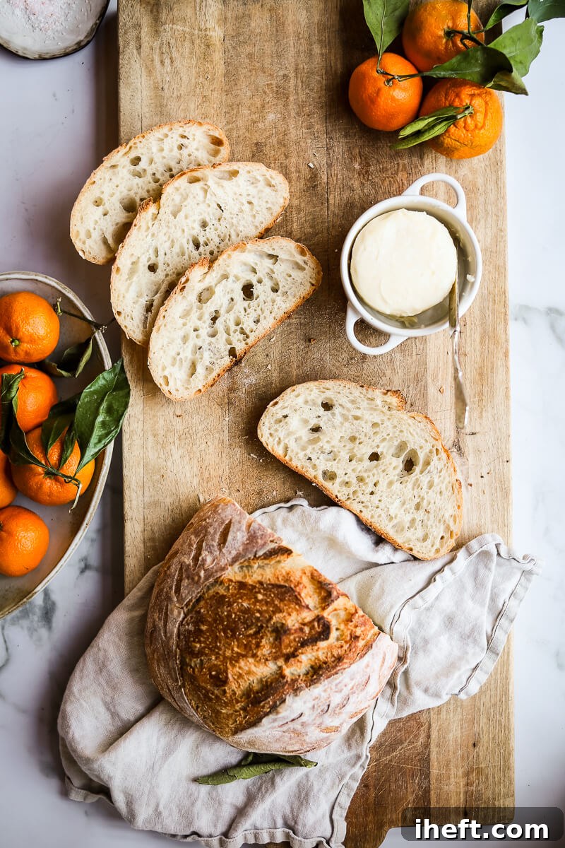 An overhead photo of homemade high hydration sourdough bread with four slices cut on on a cutting board styled with butter and satsuma tangerines.