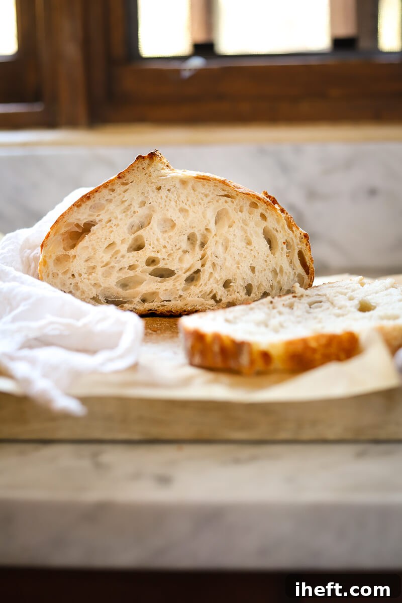Half of a loaf of homemade high hydration sourdough bread on a marble kitchen counter showing a crusty exterior and open crumb interior.