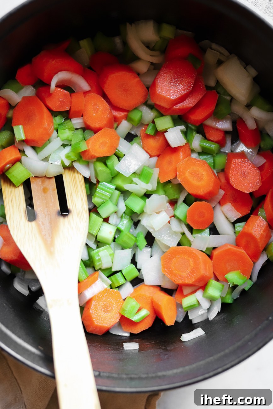 Carrots, celery, and onions saute in a pot with a wooden spoon to begin making a healthy gluten free chicken soup. 