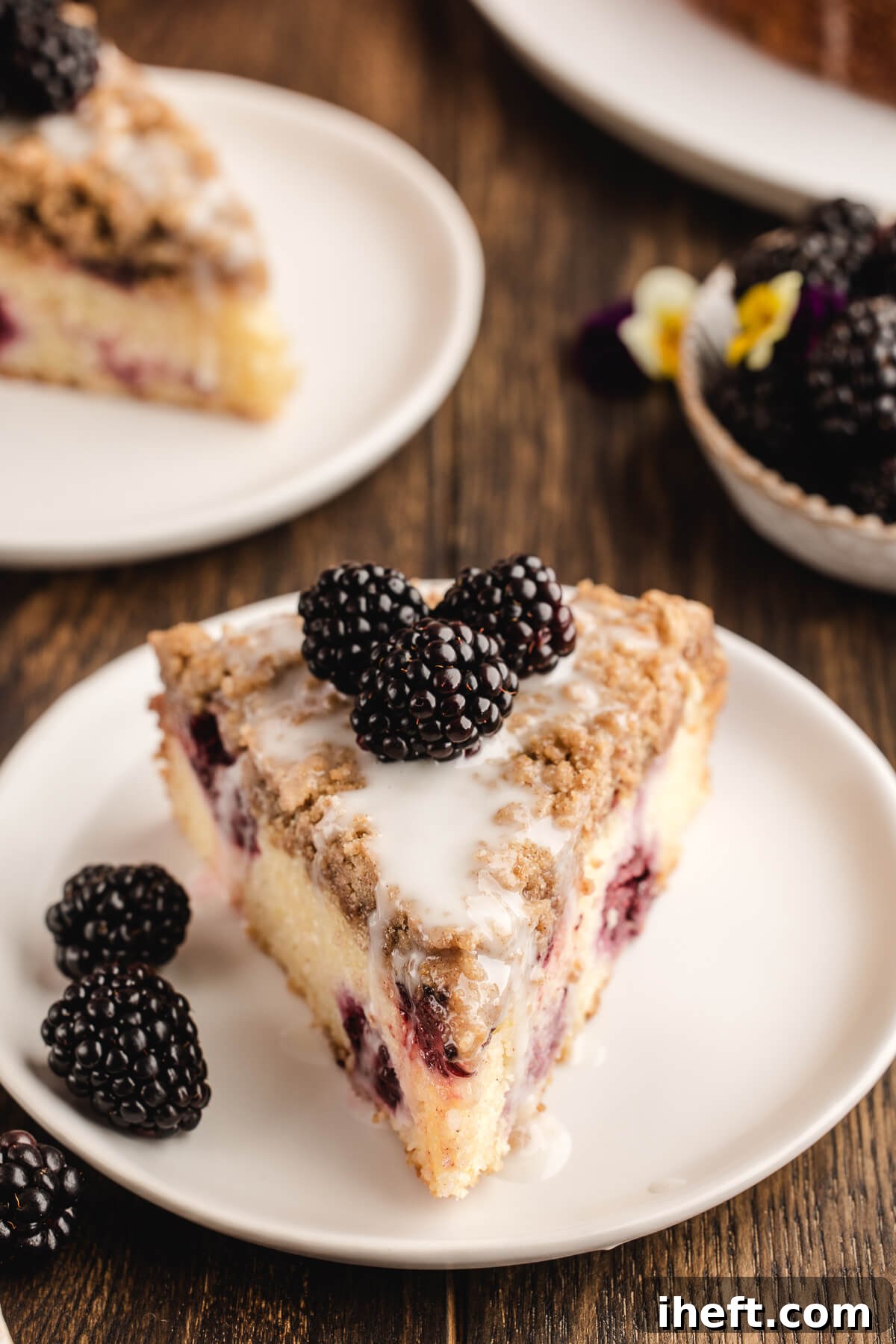 A beautifully presented slice of blackberry coffee cake with a generous streusel topping and fresh blackberry garnish on a pristine white plate, suggesting a delightful breakfast or brunch.