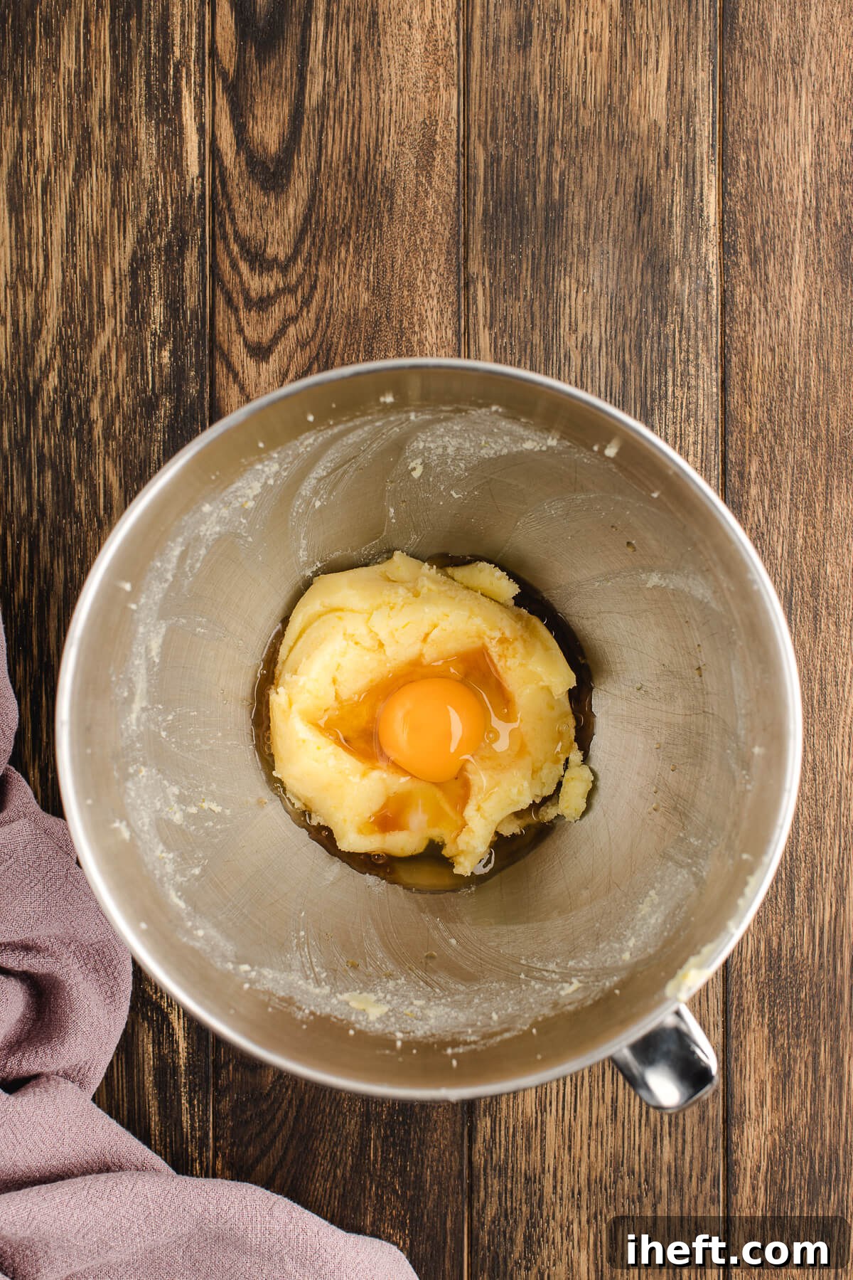 An egg is added to a stand mixer with coffee cake dough.