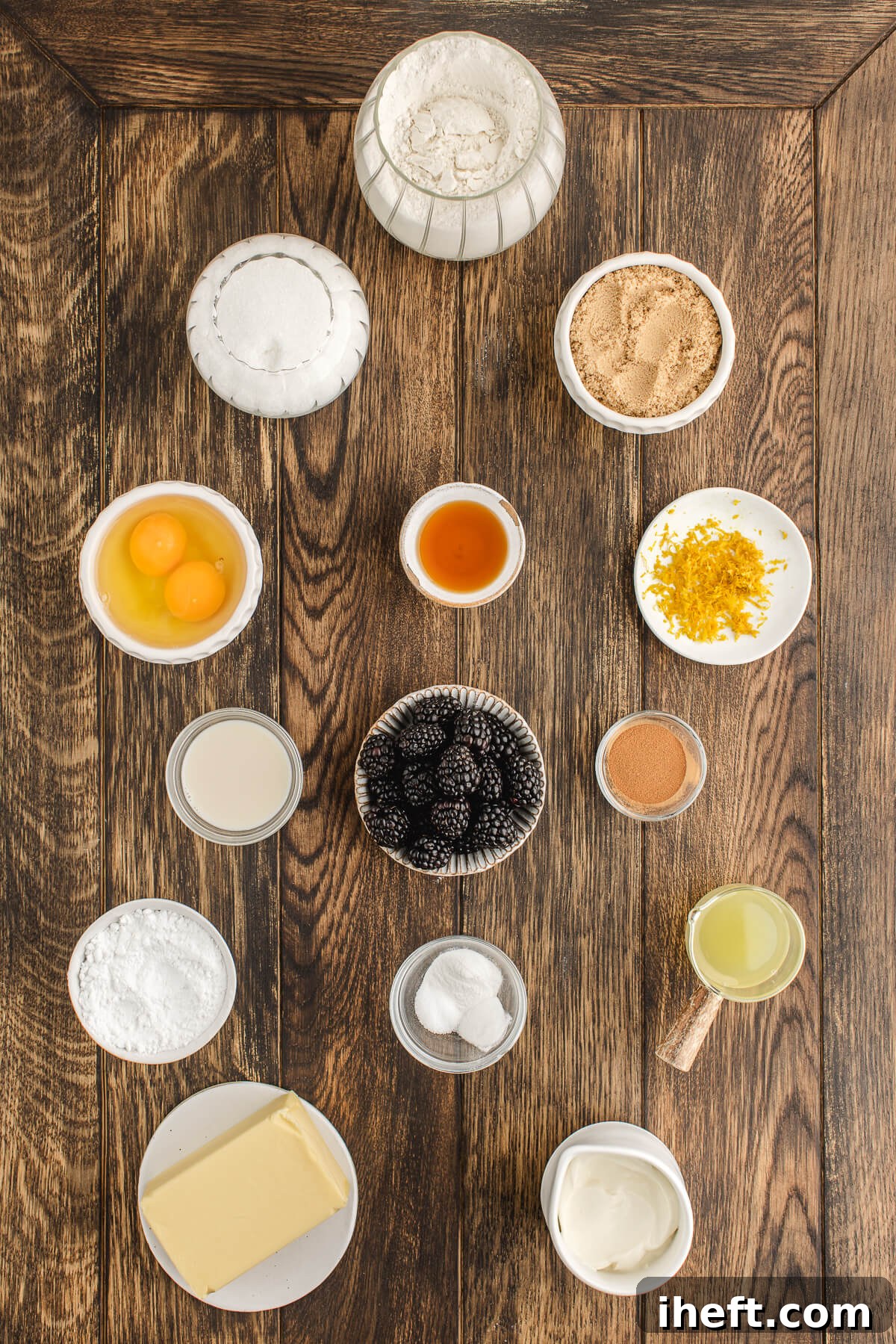 A meticulously arranged display of key ingredients for blackberry coffee cake on a rustic wooden table, including flour, brown and white sugar, vibrant lemon zest and juice, creamy sour cream, warm cinnamon, fresh blackberries, eggs, and golden butter.