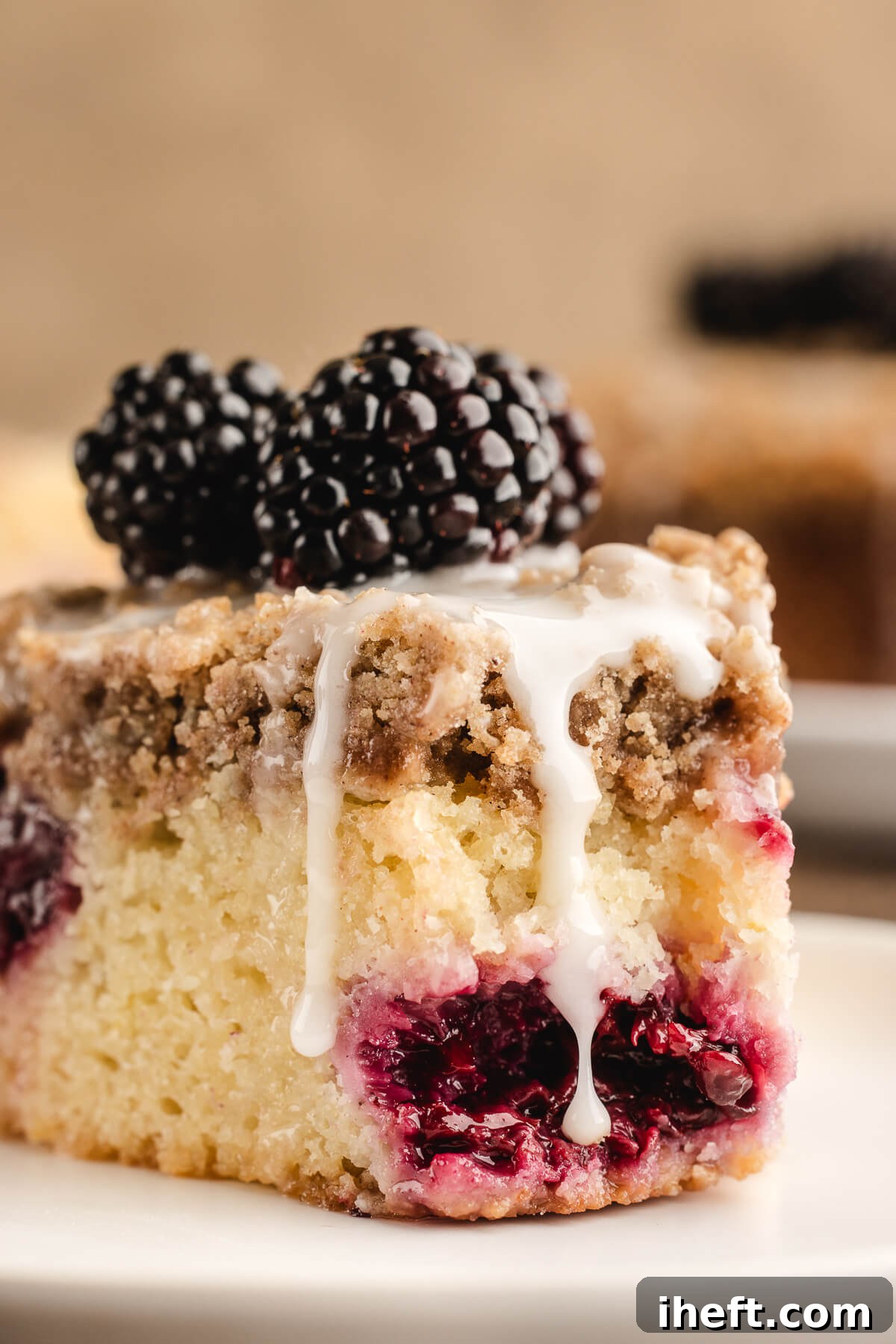 A close-up photograph showcasing the inviting interior of a slice of blackberry coffee cake, complete with a generous streusel topping, a luscious glaze, and fresh blackberries, highlighting its texture and deliciousness.
