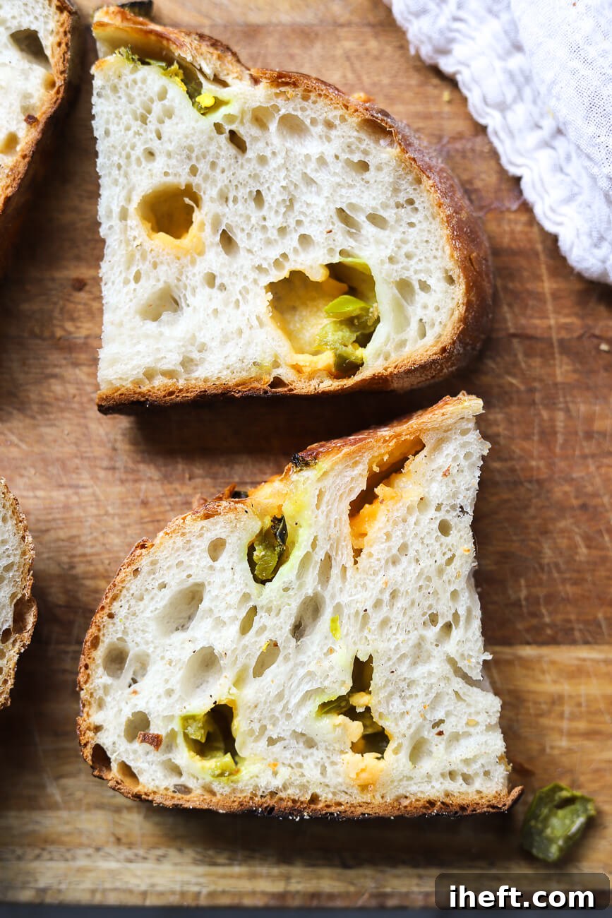 A close-up of two half-slices of jalapeno cheddar sourdough bread on a wooden cutting board. 