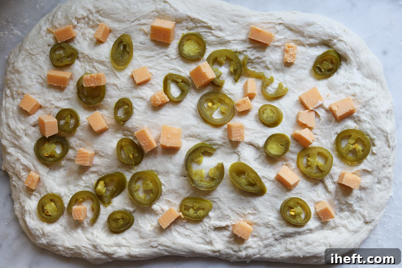 Sliced jalapenos and cheddar cheese cubes scattered on top of sourdough bread dough.