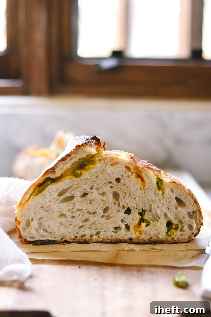 Half a loaf of Jalapeño Cheddar Sourdough with an open crumb sits on a wooden cutting board. 