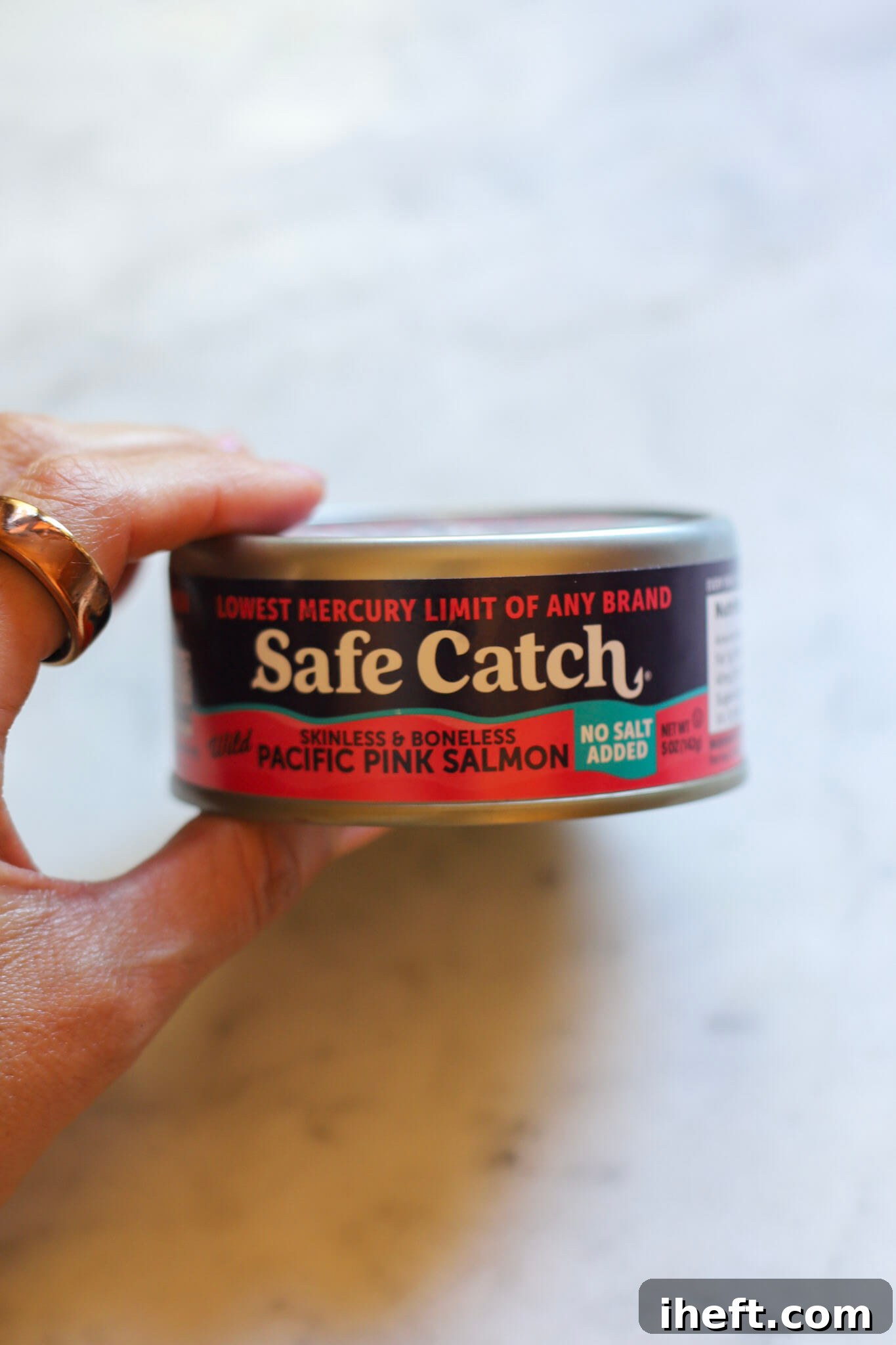 A hand holds a can of Safe Catch canned wild salmon on marble counter.