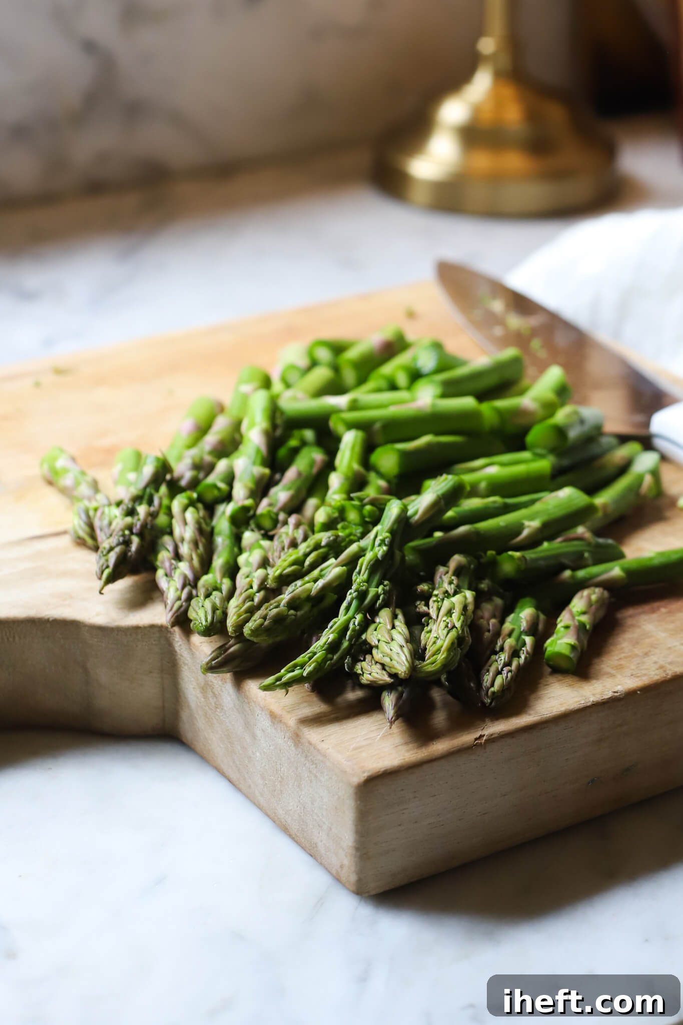Asparagus cut into pieces on a wooden cutting board on a marble kitchen counter before making an asparagus salad. 