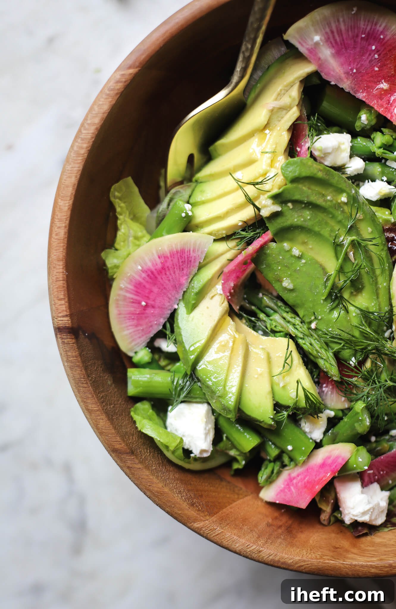 A close up of a beautiful asparagus salad with greens, avocado, watermelon radish, dill, and feta. 