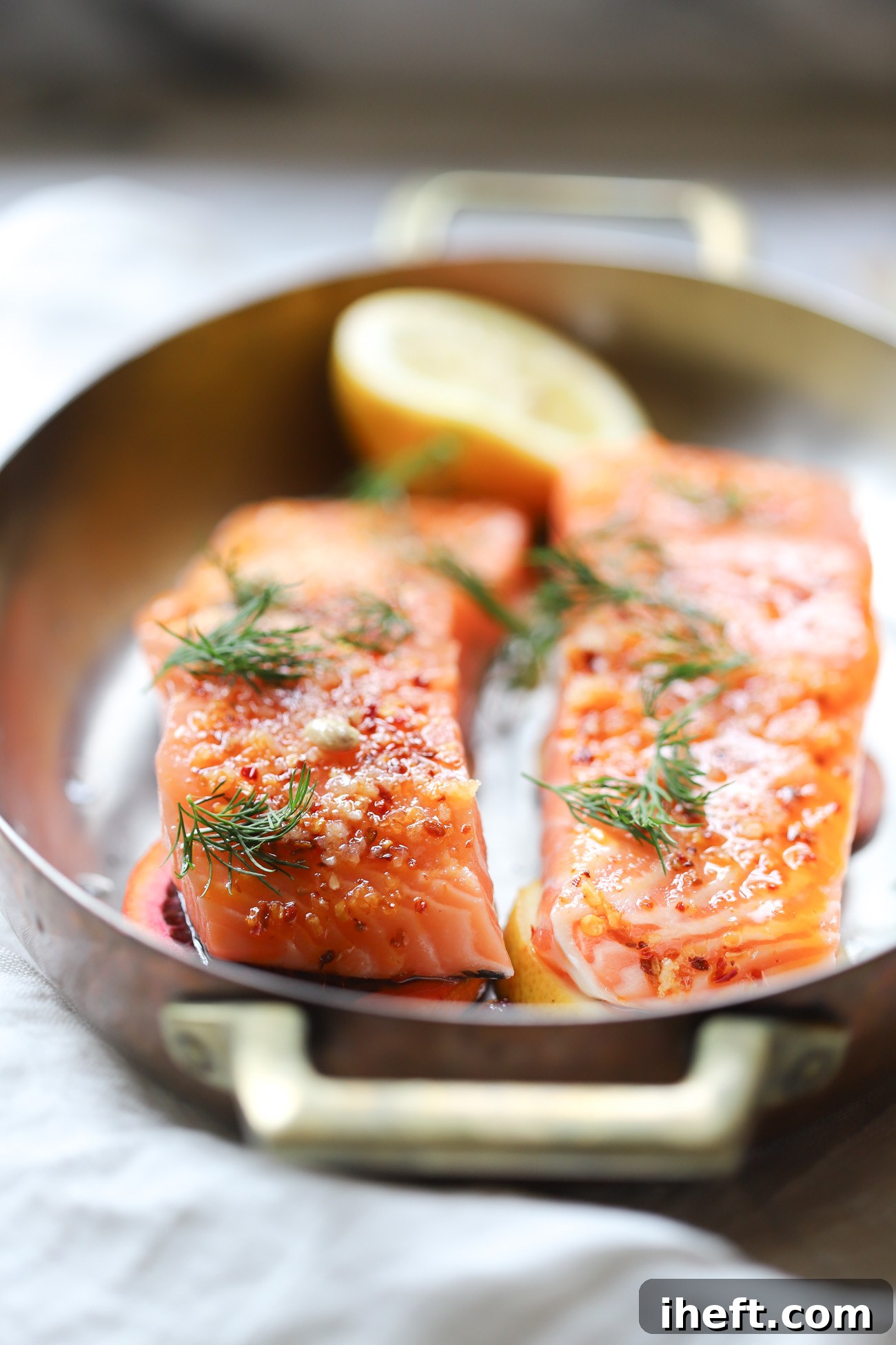 Two raw wild salmon filets in an oval baking dish topped with chili onion crisp and fresh dilll. 