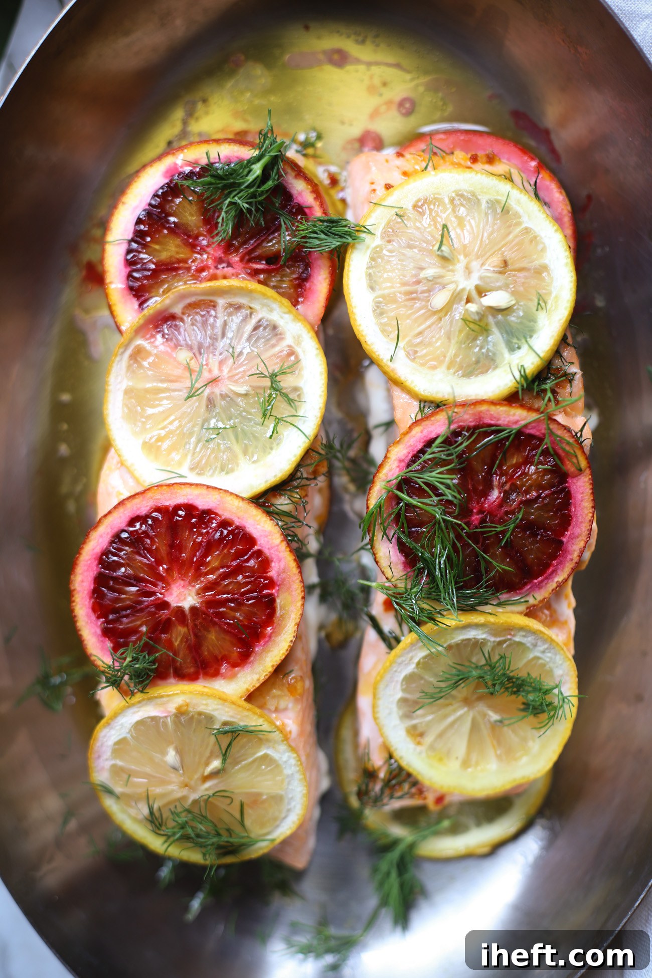 An overhead close-up photo of two salmon filets that have been baked topped with slices of blood orange, lemon, and dill. 