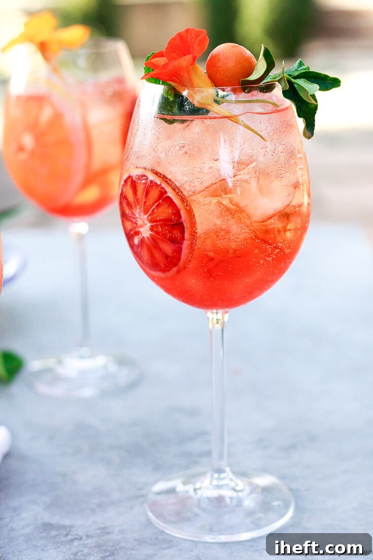 A beautiful Aperol spritz in a wine glass garnished with Nasturtium flowers and citrus.