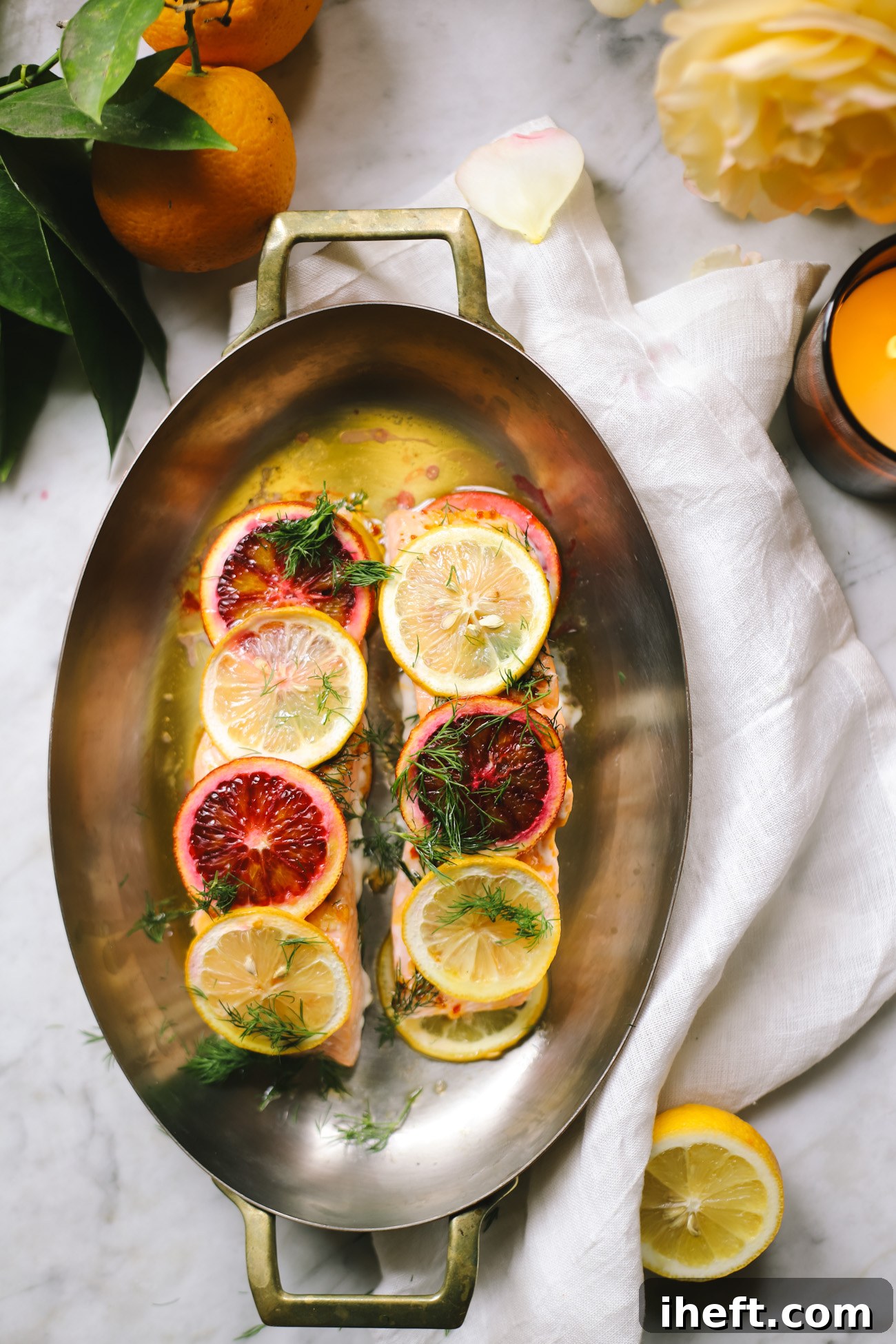 Two baked salmon filets topped with lemon and blood orange slices on a marble countertop.