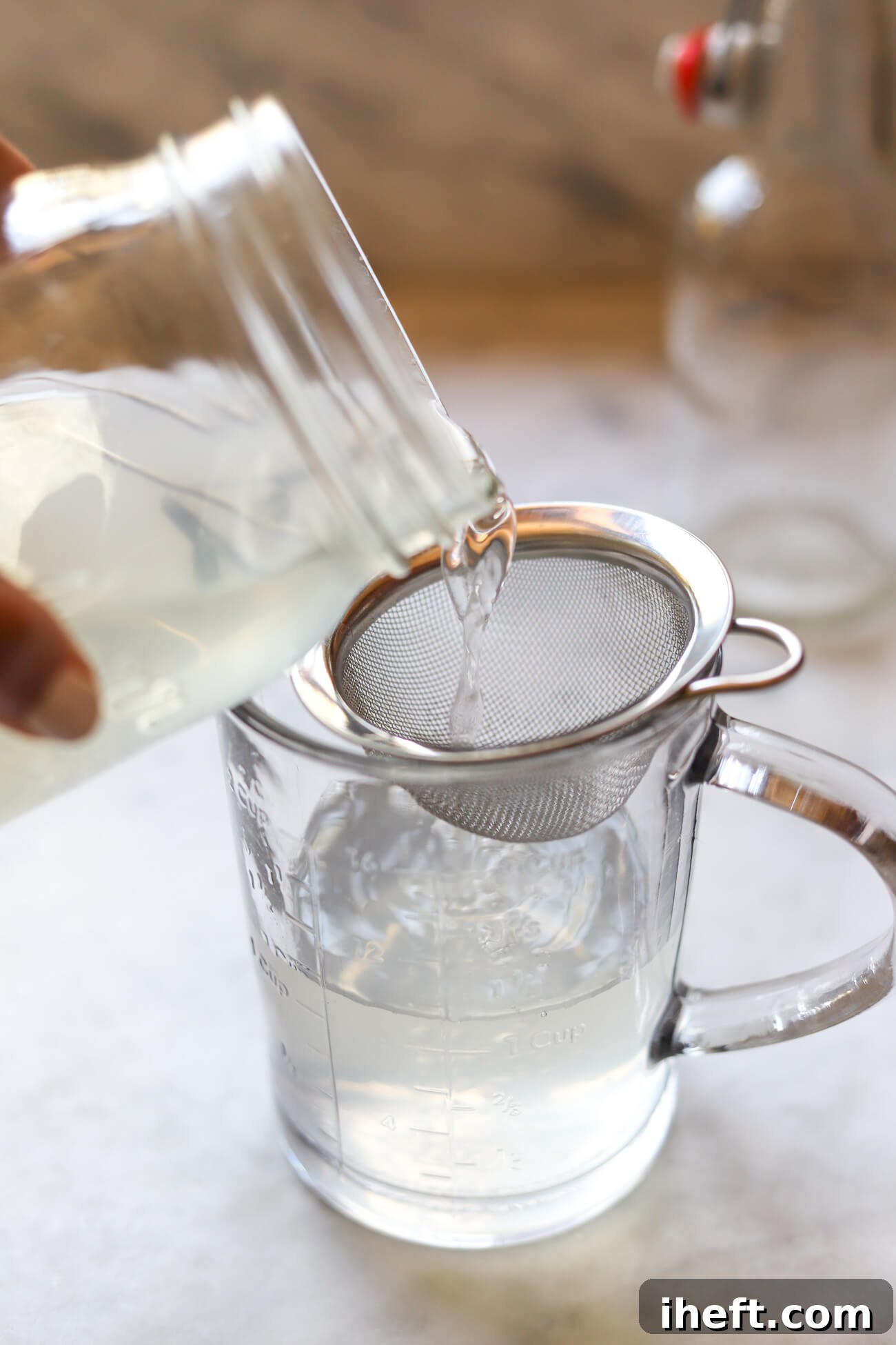 Water kefir grains are strained out of the liquid through a fine mesh sieve into a large pouring measuring cup after the first ferment is finished.