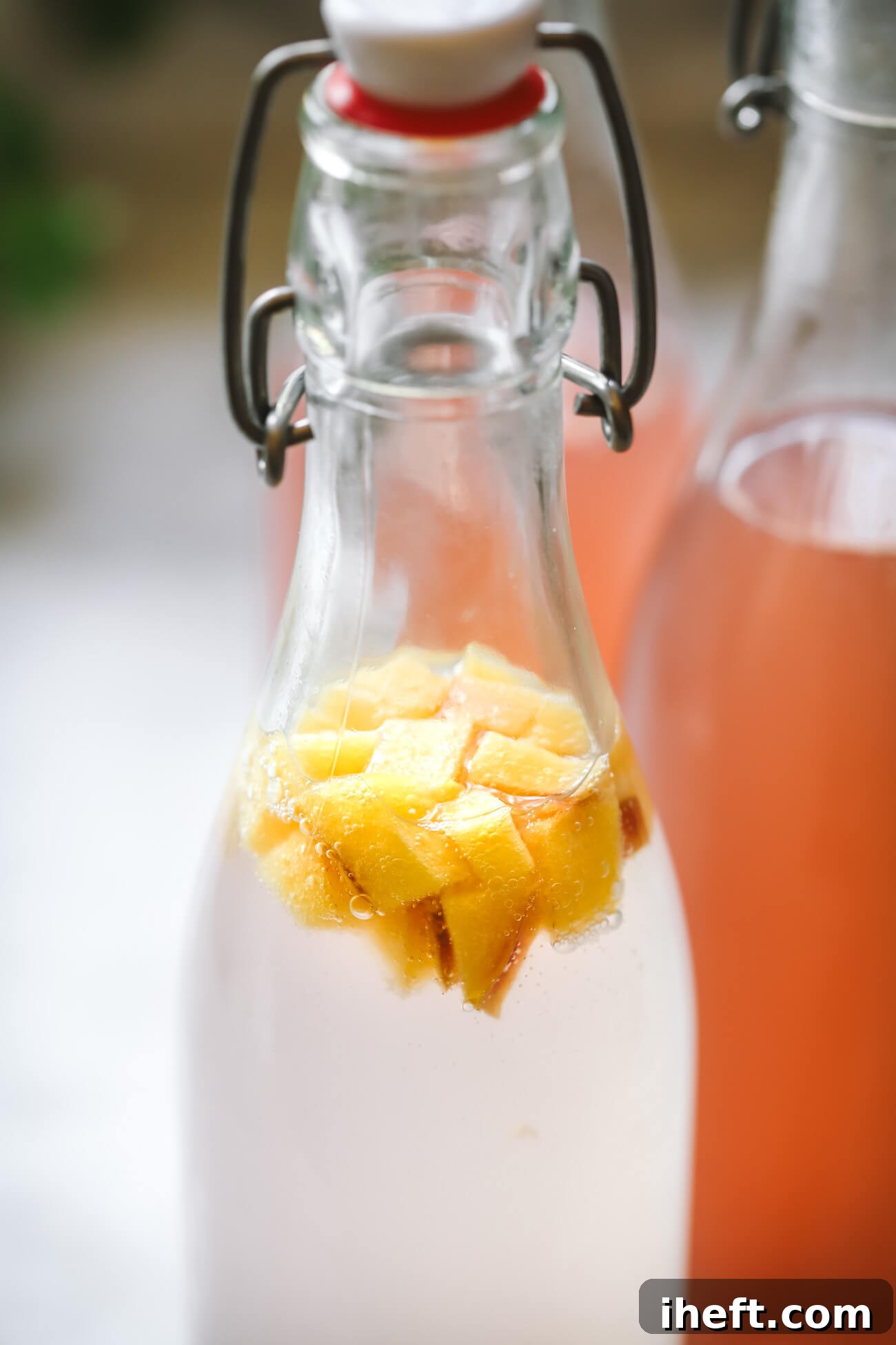 A close-up photo of a swing top bottle filled with fermenting water kefir and diced peaches.