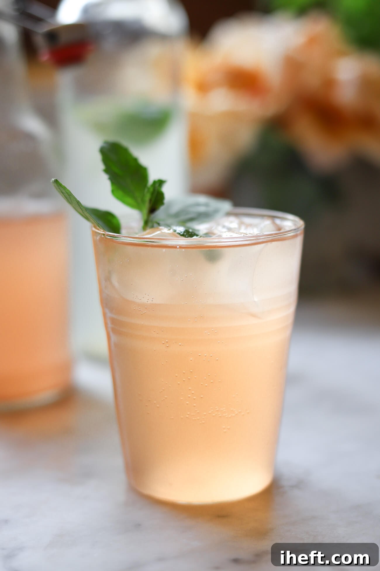 A close-up of a glass filled with ice and agua de kefir or water kefir garnished with fresh mint on a marble kitchen counter.