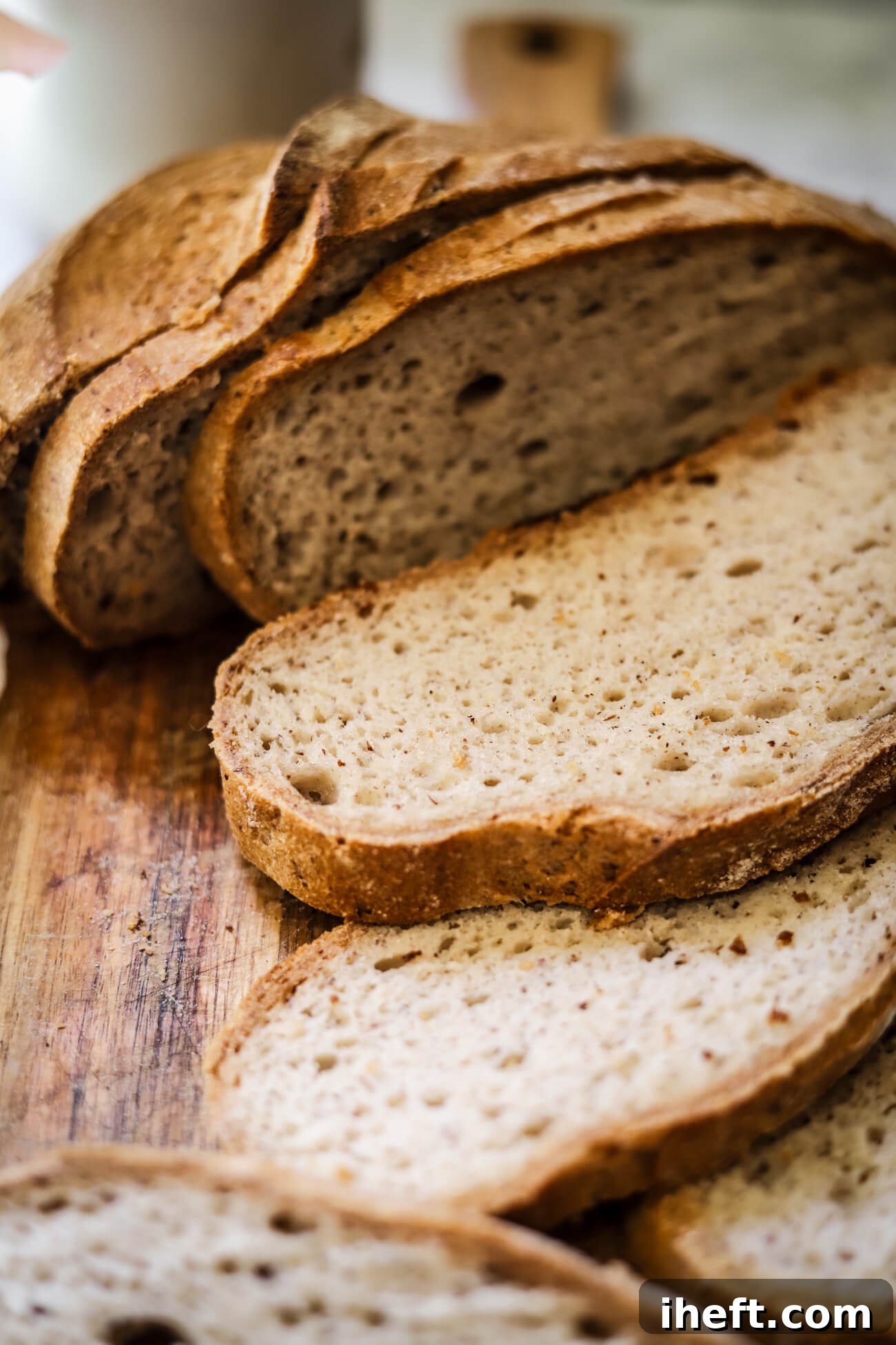 Close-up food photography of a homemade gluten free sourdough bread cut into slices on a wooden cutting board. This photo shows bread with a dark golden crust and light, airy, open crumb interior. 