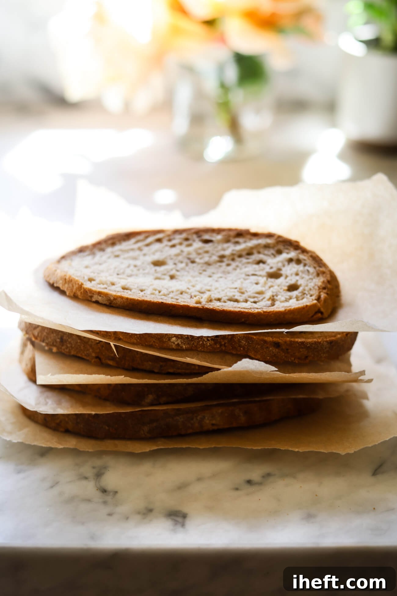 Slices of homemade sourdough bread separated by sheets of parchment paper are ready to be frozen. 