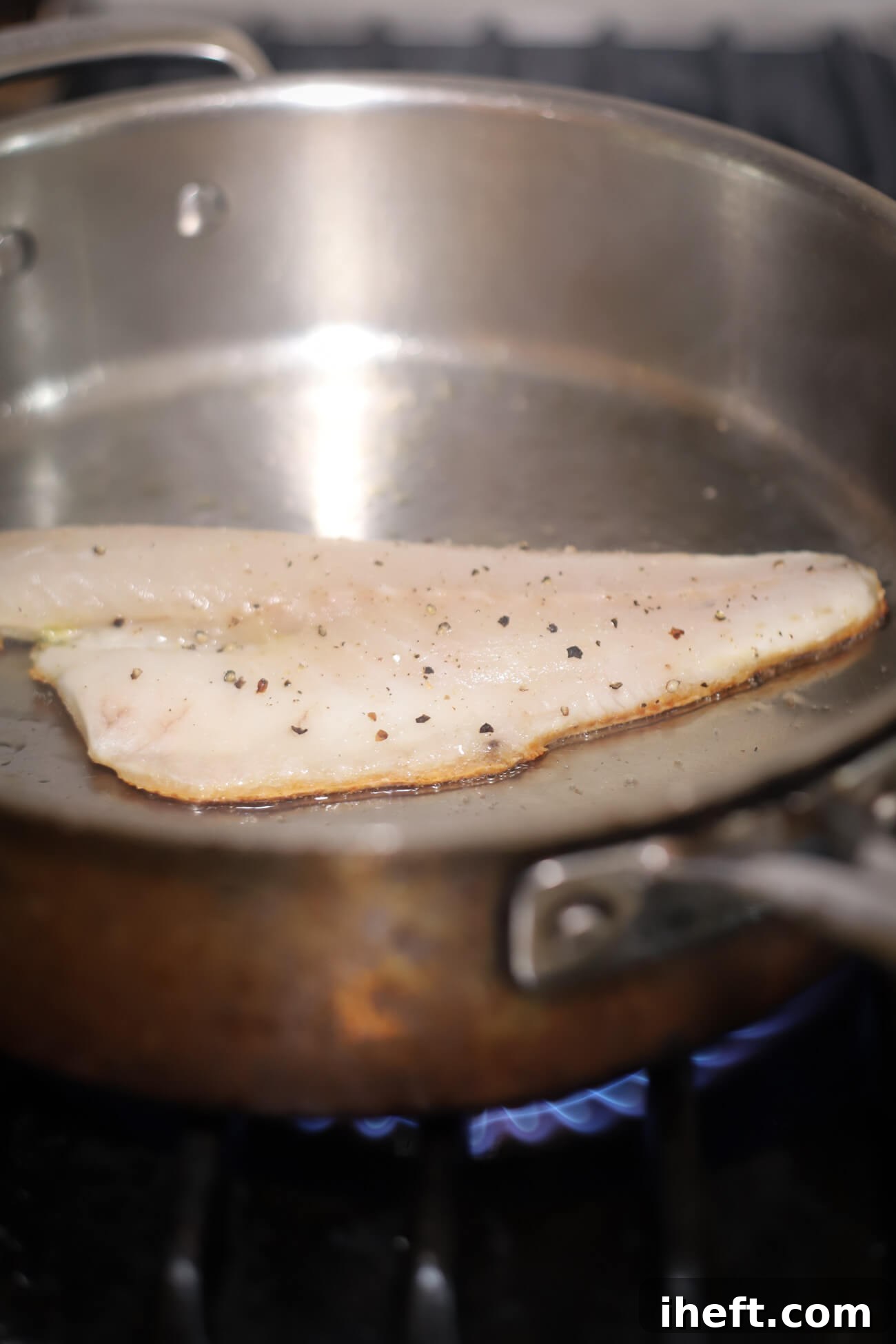 A branzino fillet sizzling in a stainless steel skillet, its skin crisping to a beautiful golden brown as it pan-sears, highlighting the key cooking process for perfect texture.