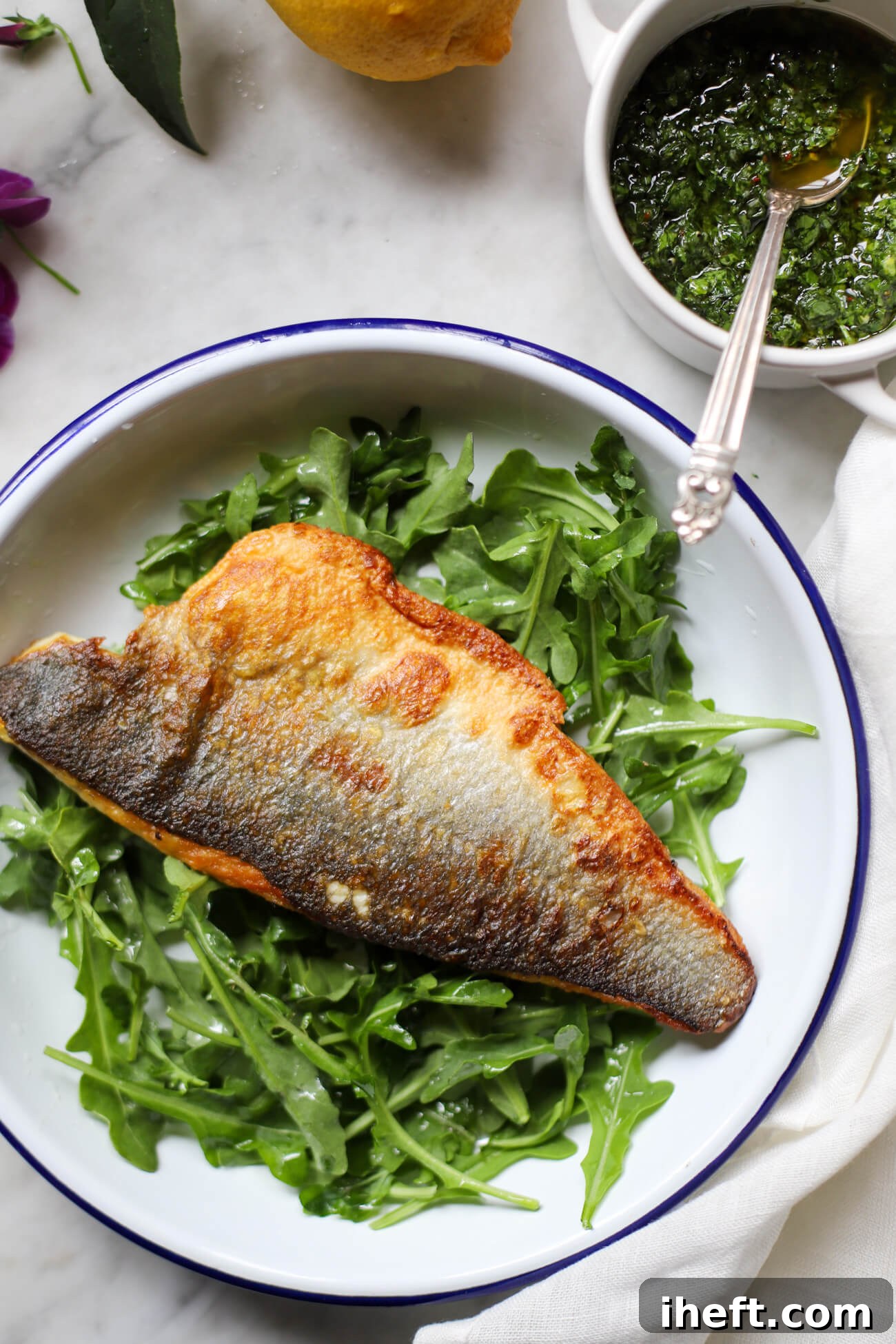 A perfectly cooked fillet of crispy skin branzino, skin-side-up, elegantly presented on a bed of fresh arugula alongside a small, vibrant dish of gremolata, ready to be enjoyed.