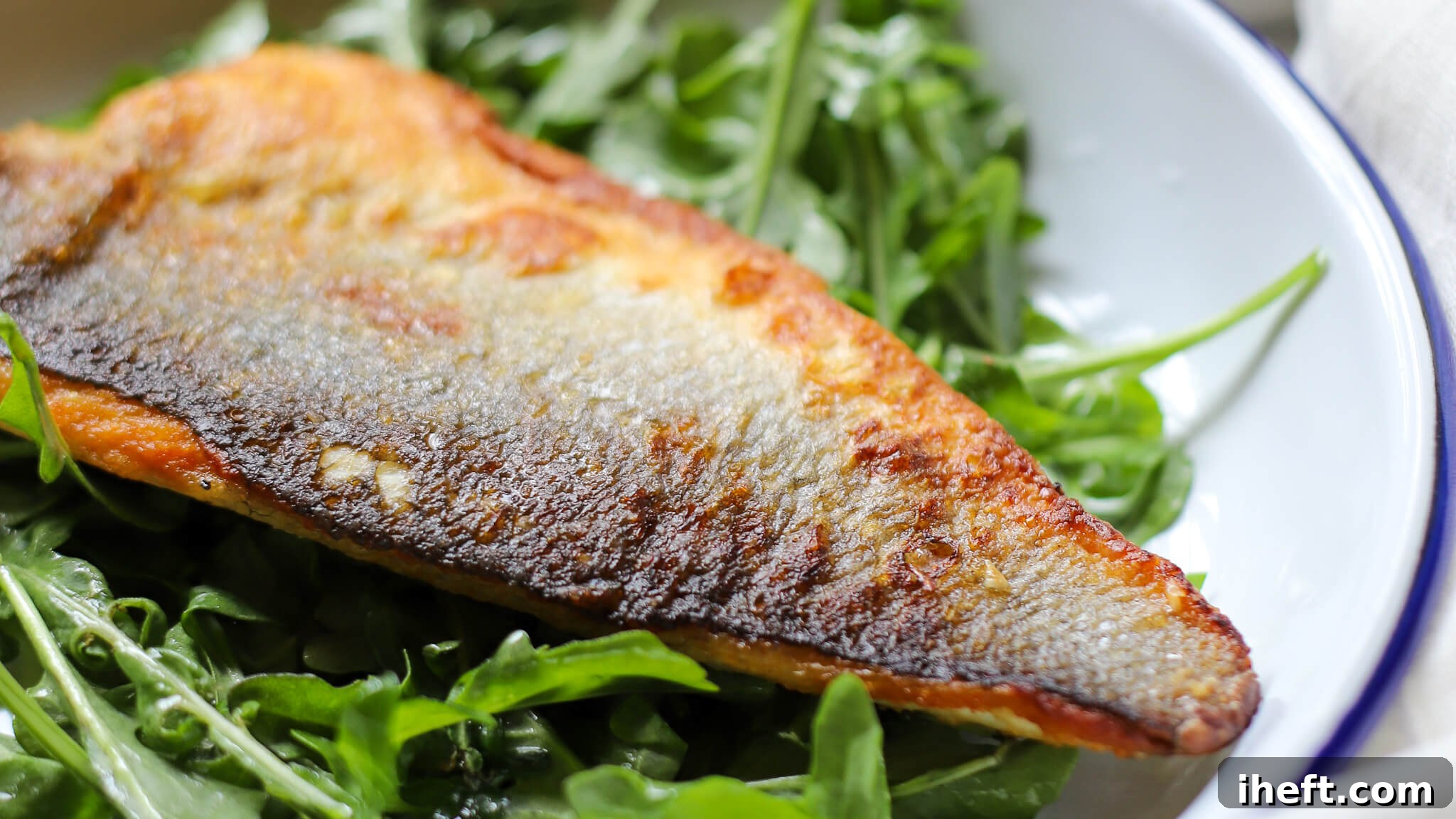 A fillet of crispy skin branzino resting on a bed of fresh arugula, showcasing its perfect doneness.