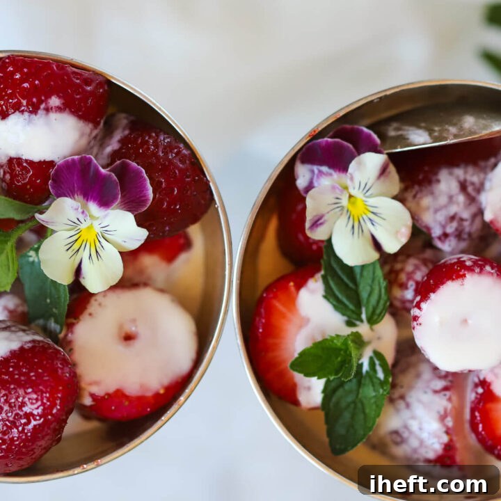 An overhead photo of two silver coupes filled with Wimbledon style strawberries and cream garnished with mint and violas.