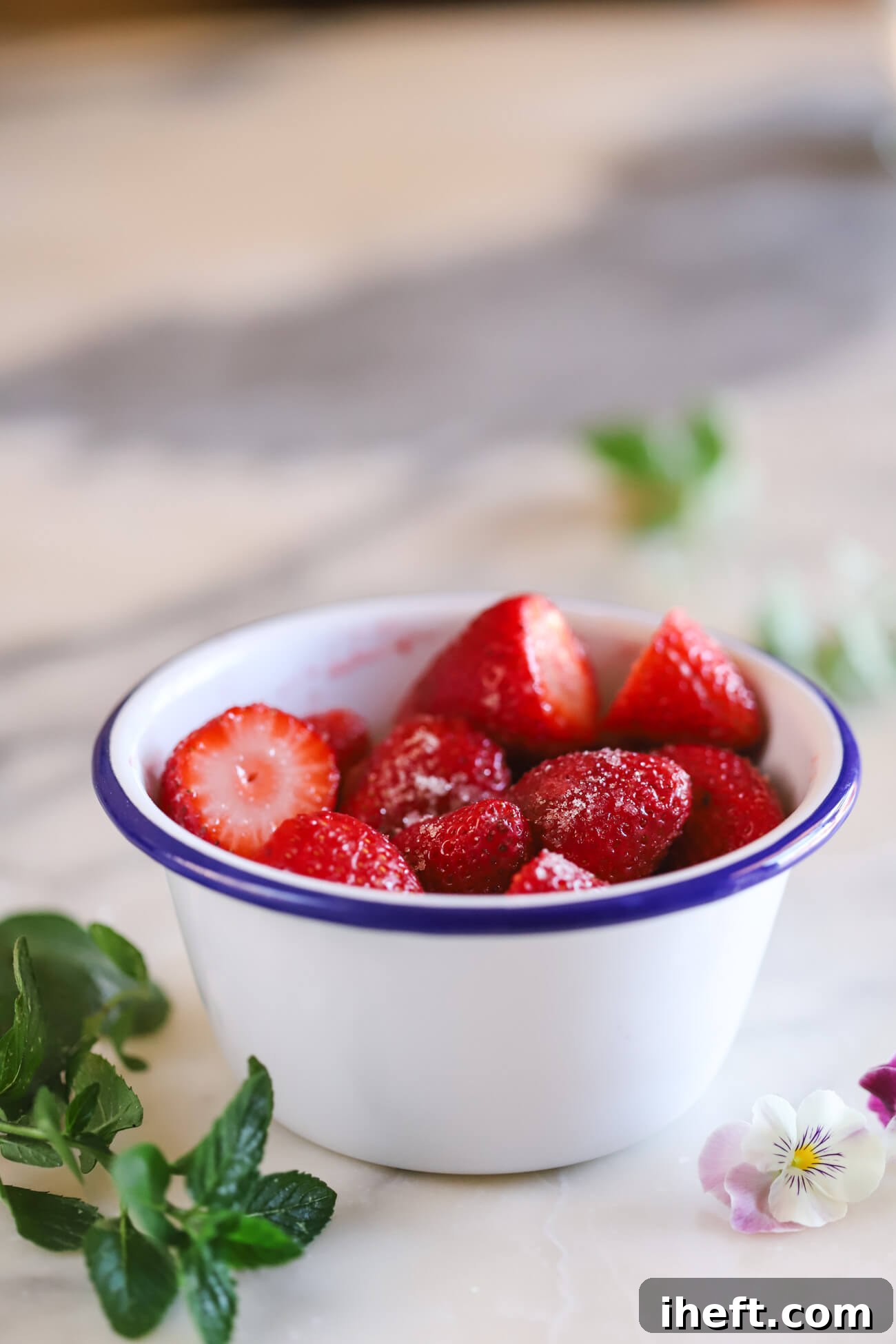 A white bowl with blue rim filled with strawberries lightly coated in sugar to macerate.
