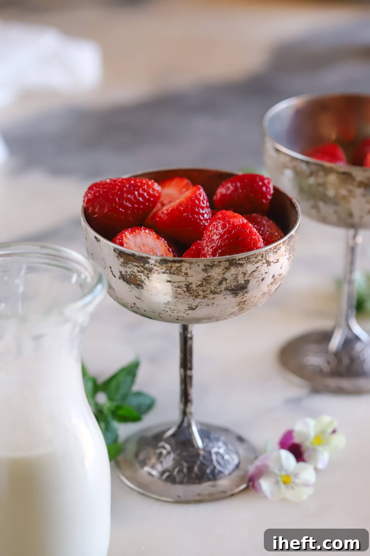 A vintage silver coupe glass willed with sugar coated strawberries with a small juice jar of cream in the foreground to make Wimbledon strawberries and cream.