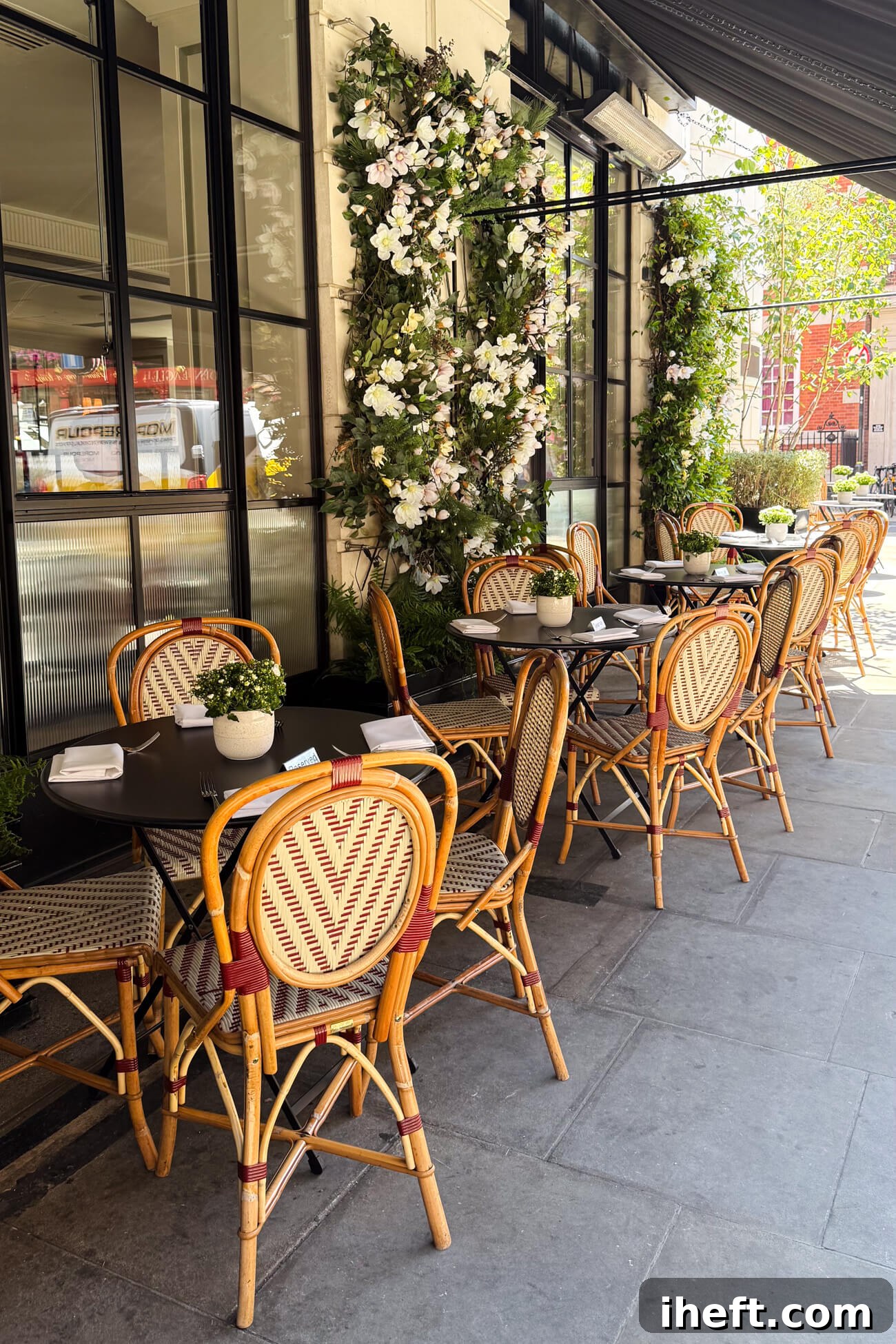 Picturesque outdoor French style bistro dining tables and chairs on a flower-lined sidewalk at the Marylebone Hotel. This is the outdoor dining area for 108 Brasserie. 