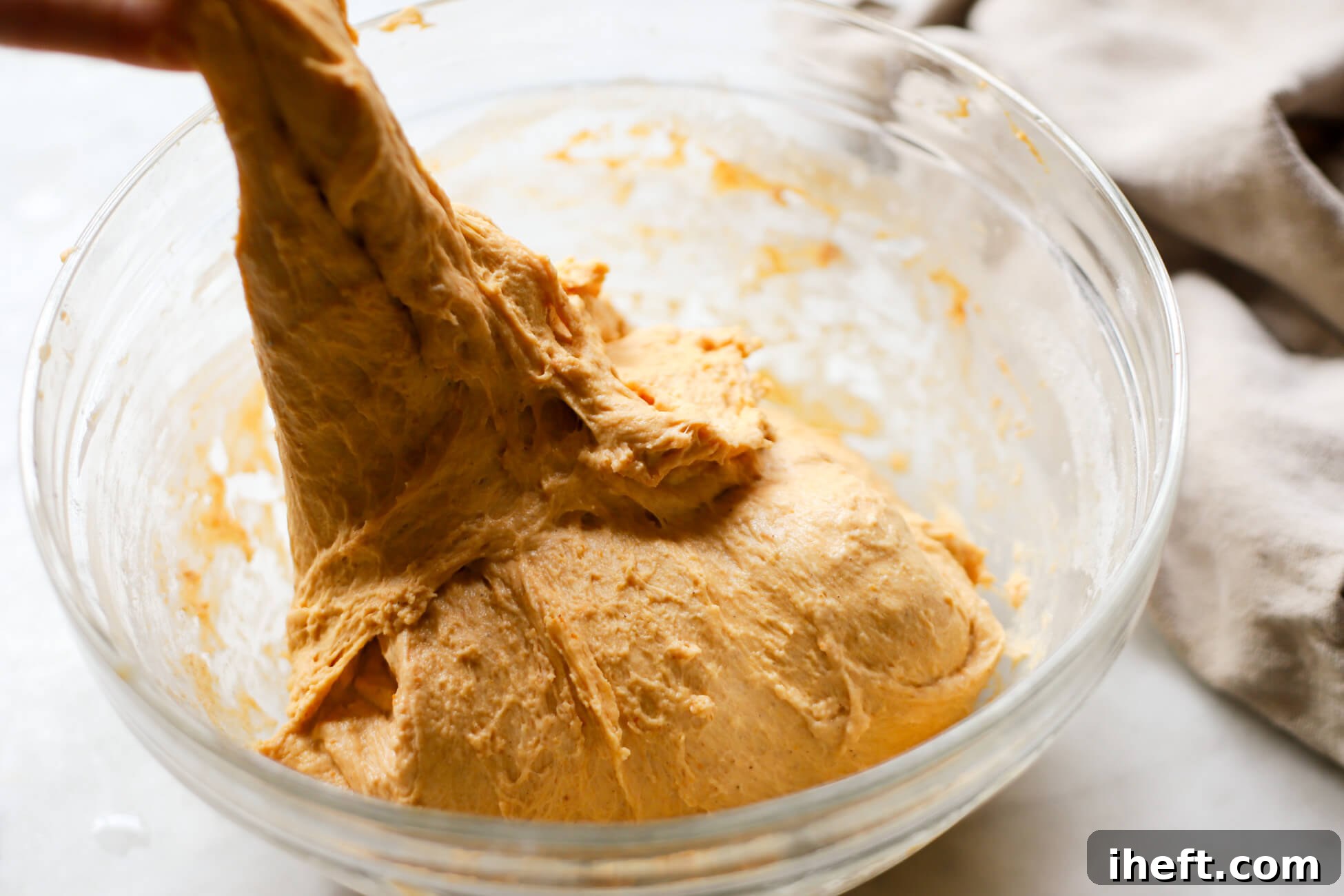 Pumpkin sourdough dough is pulled up from a glass bowl to perform "stretch and folds."