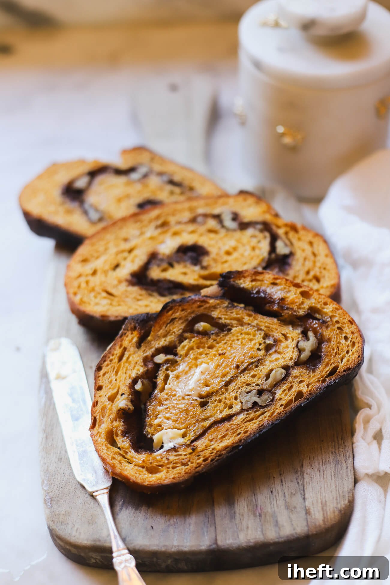 Toasted slices of pumpkin sourdough bread with cinnamon sugar swirl and walnuts on a wooden board with butter knife