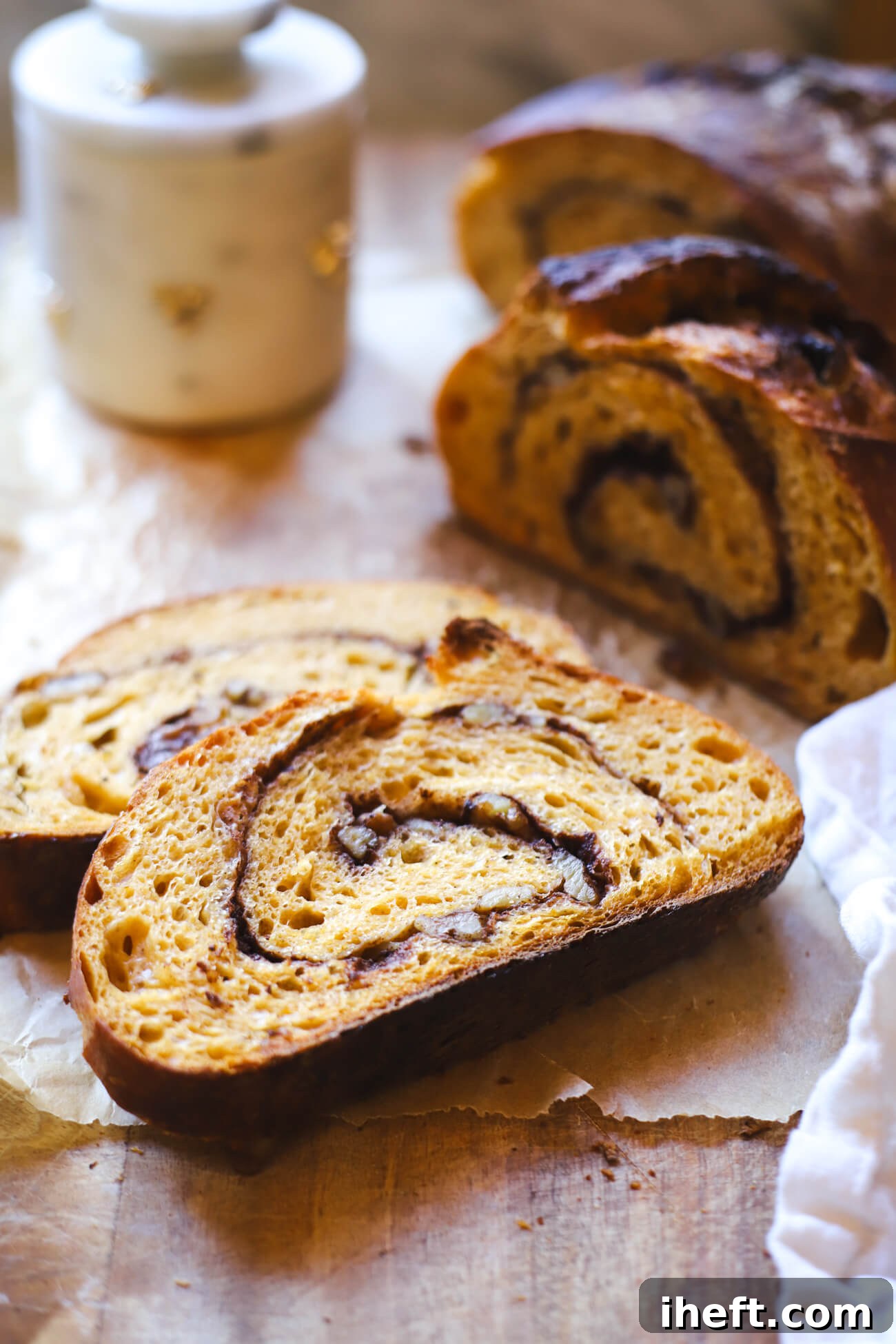 Sliced pumpkin sourdough bread showing cinnamon sugar swirl and walnuts on parchment paper