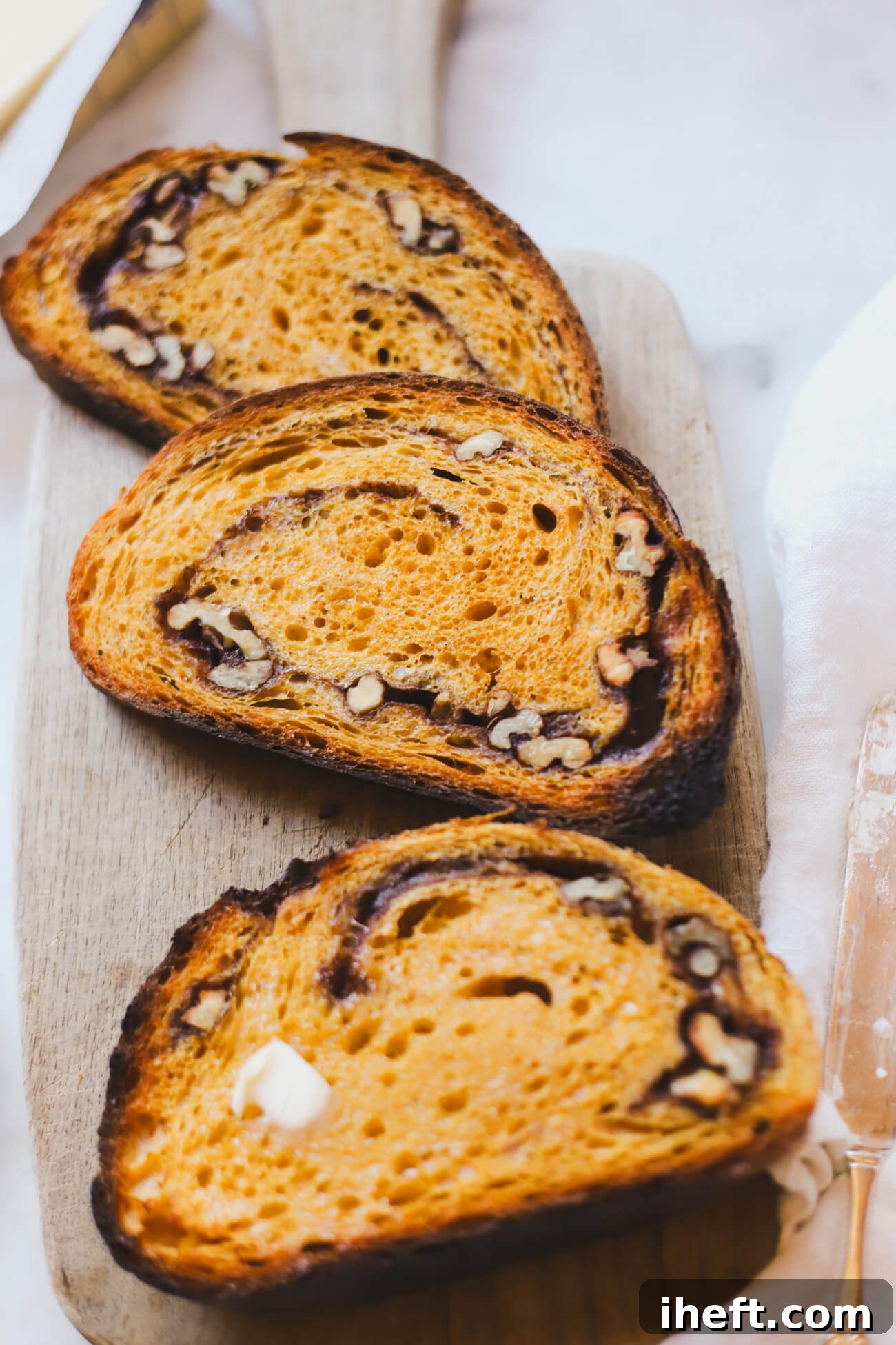 3 slices of beautiful toasted pumpkin spice sourdough bread with cinnamons swirl and walnuts on a wooden cutting board. 