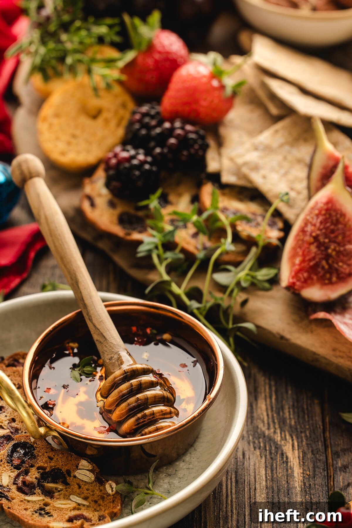 Beautiful close-up food photography of a small copper dish of hot honey with a wooden dipper in front a charcuterie grazing board. 