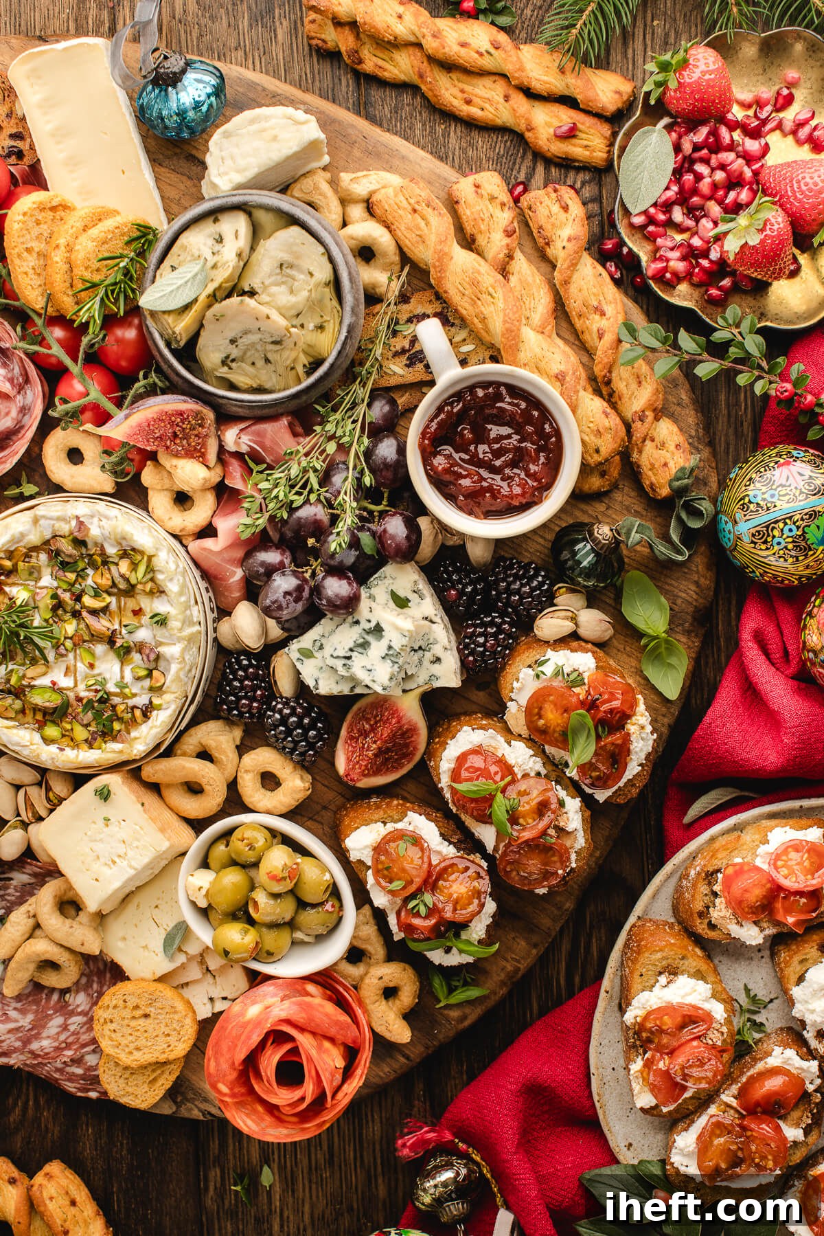 Close-up of a Christmas charcuterie board with brie, olives, salami, crackers, fresh figs, tomato crostini, grapes, and holiday greenery.