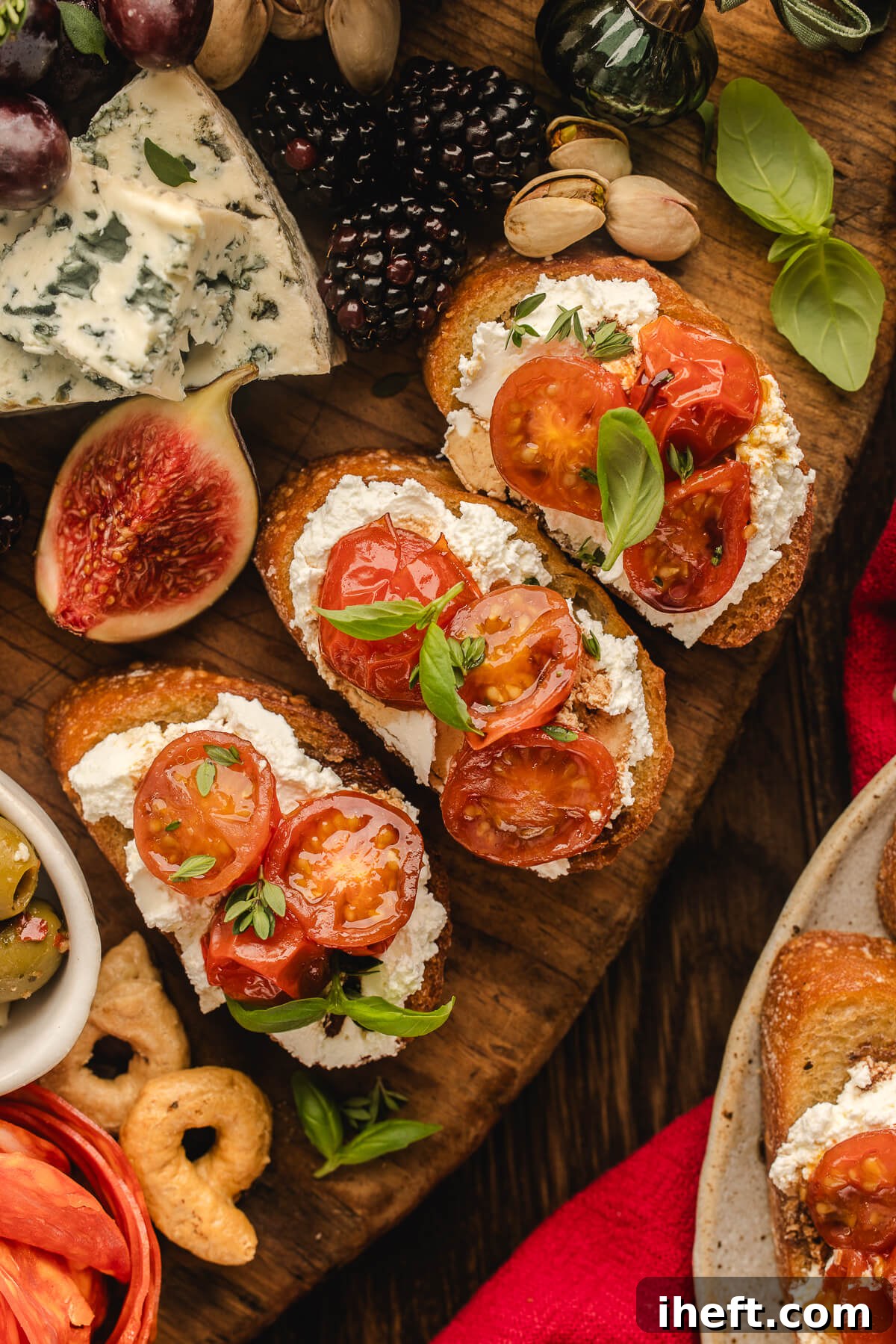 Close-up of charcuterie grazing table with crostini topped with whipped ricotta, roasted tomatoes and basil with other grazing board ingredients.