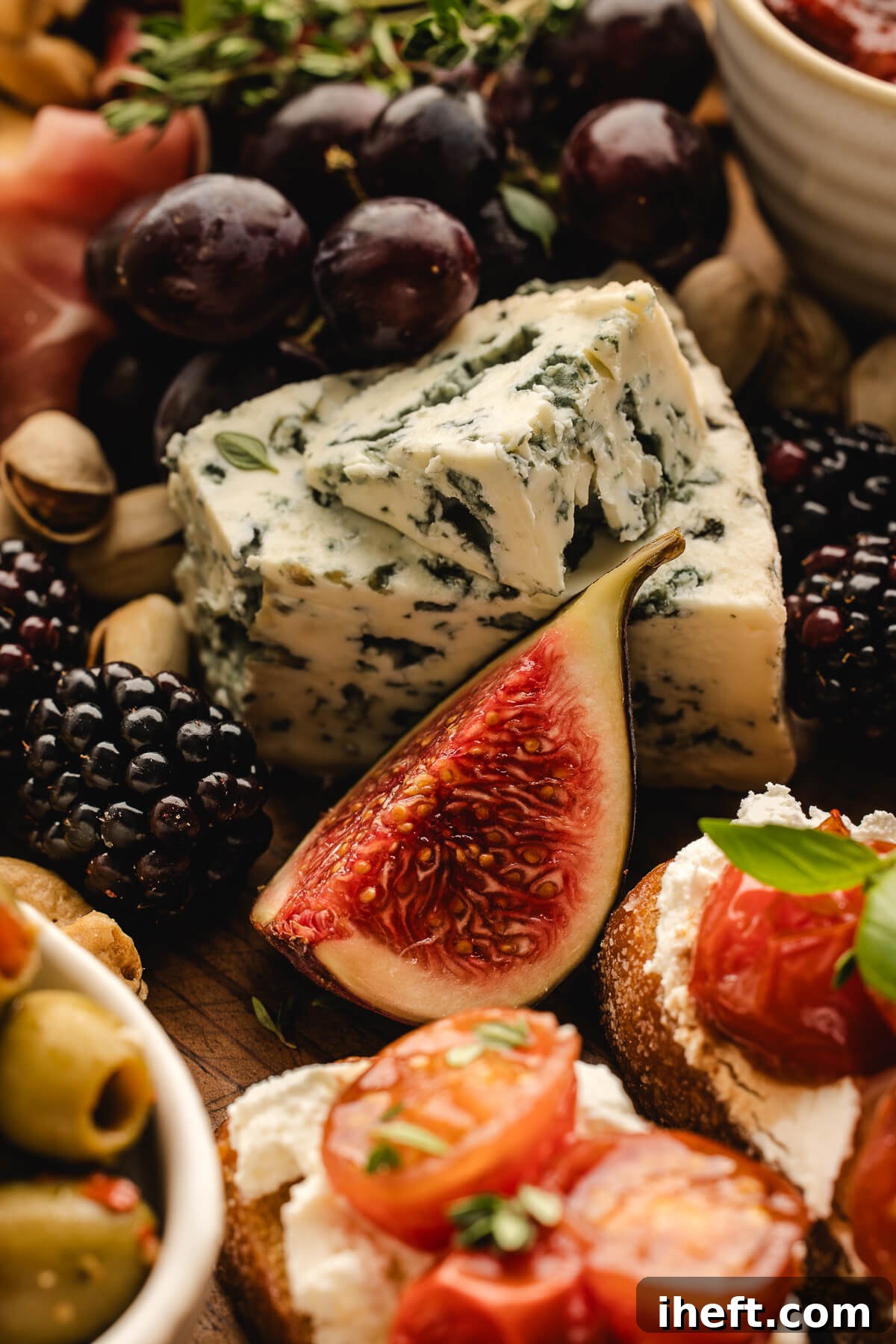 Close up-food photography of a fig, piece of bleu cheese, grapes, berries, olives, and a whipped ricotta crostini as part of a charcuterie board. 