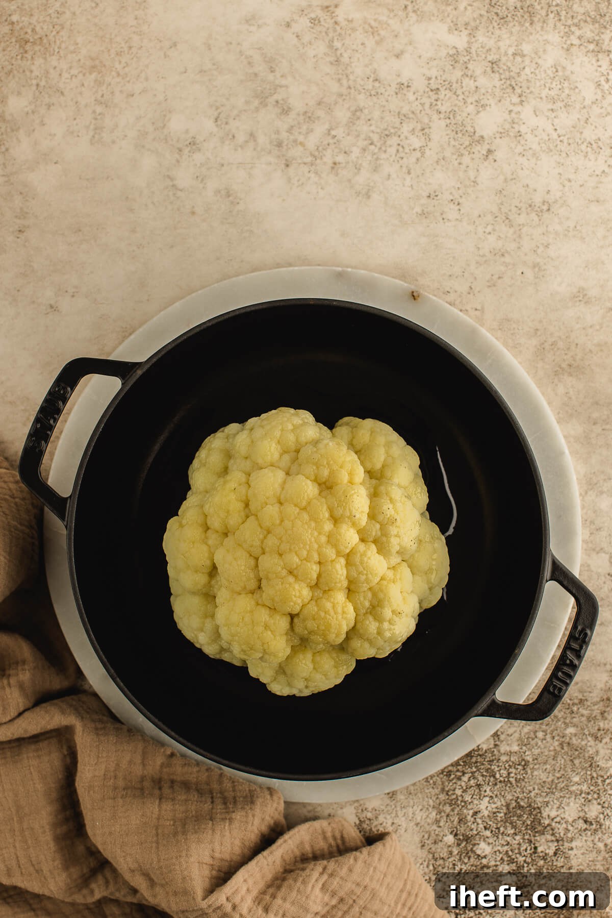 A whole cauliflower on a steamer rack in a Staub cast iron pot, ready for parboiling.