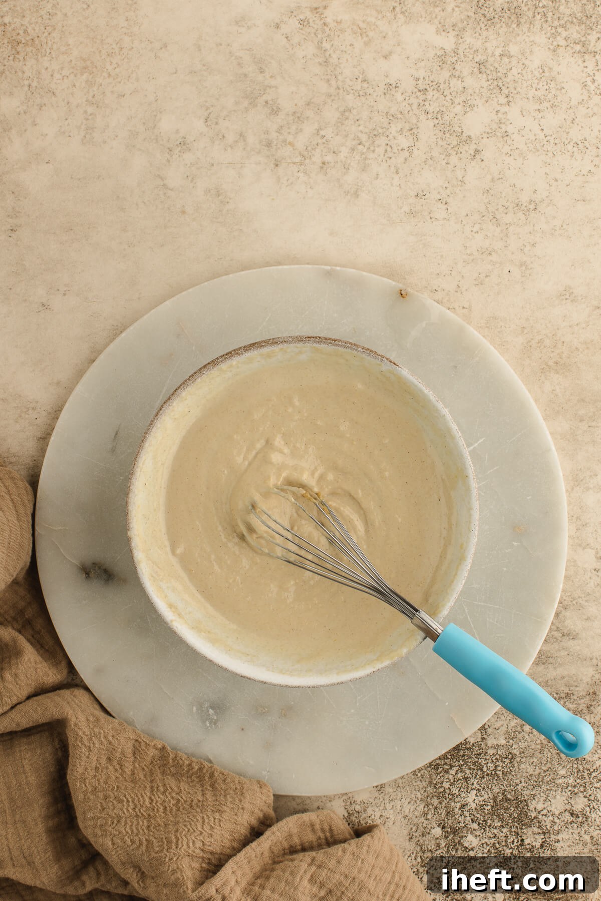 Homemade tahini sauce being prepared in a ceramic bowl with a small whisk, showcasing its creamy texture.