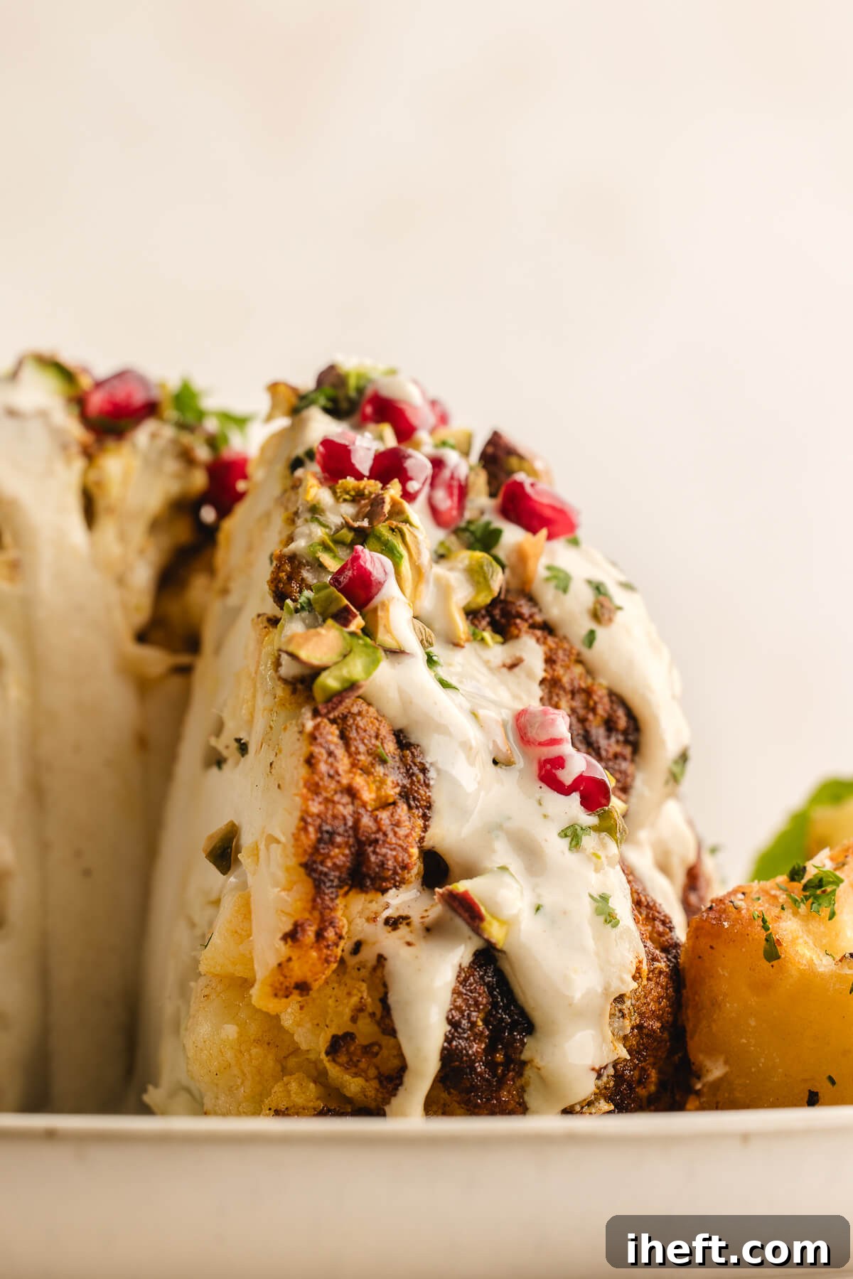 A beautifully presented whole roasted cauliflower with a wedge thoughtfully removed, showcasing its tender interior and delectable toppings.