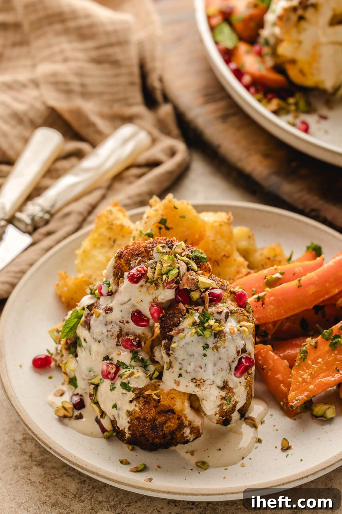 Plated serving of whole roasted cauliflower with tahini sauce, pistachios, pomegranate seeds, and roasted carrots — an elegant vegetarian holiday meal.