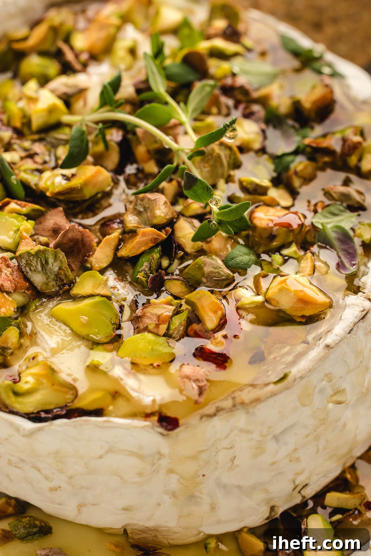 Close-up of hot honey baked Brie overflowing with melted cheese, pistachios, and fresh thyme, served on a rustic board.