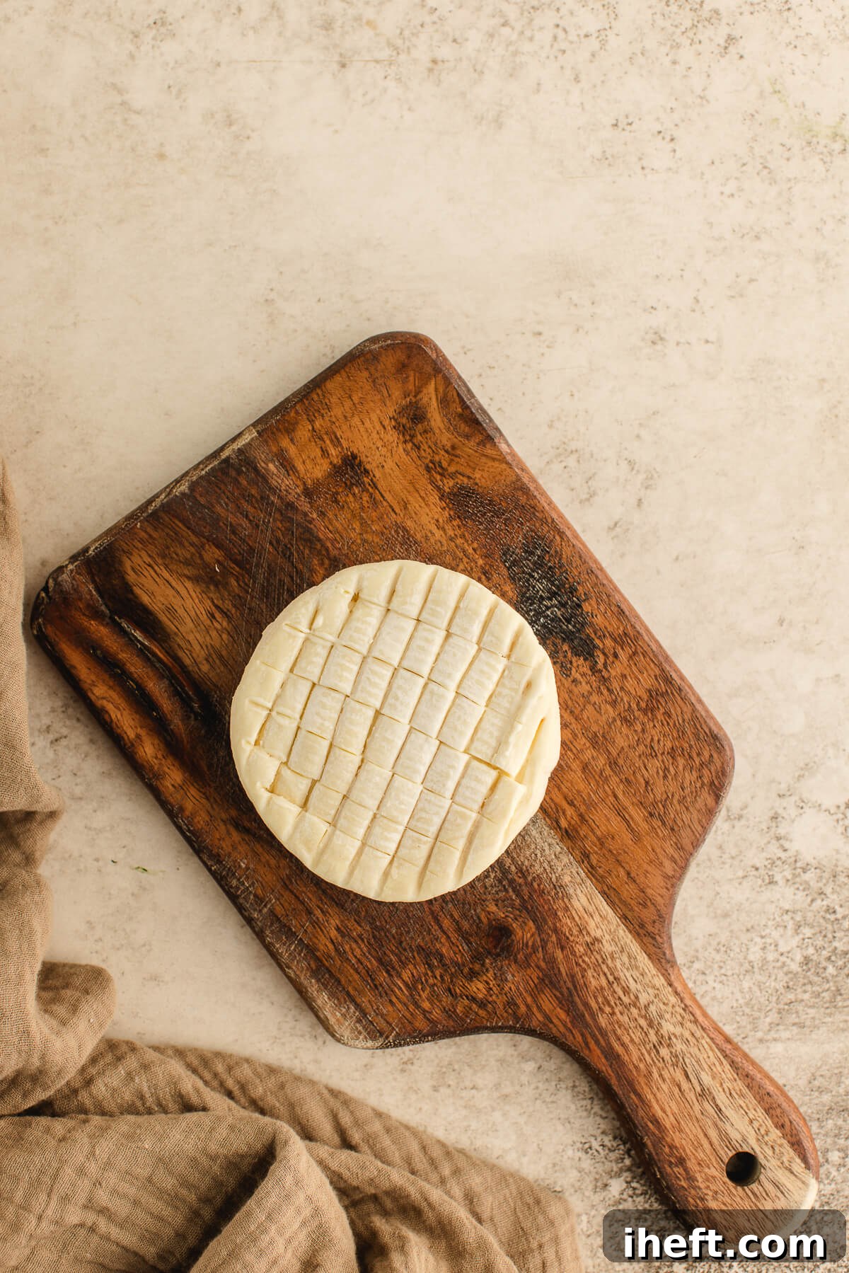 Scored wheel of Brie on a wooden cutting board, ready to bake for an easy holiday appetizer.
