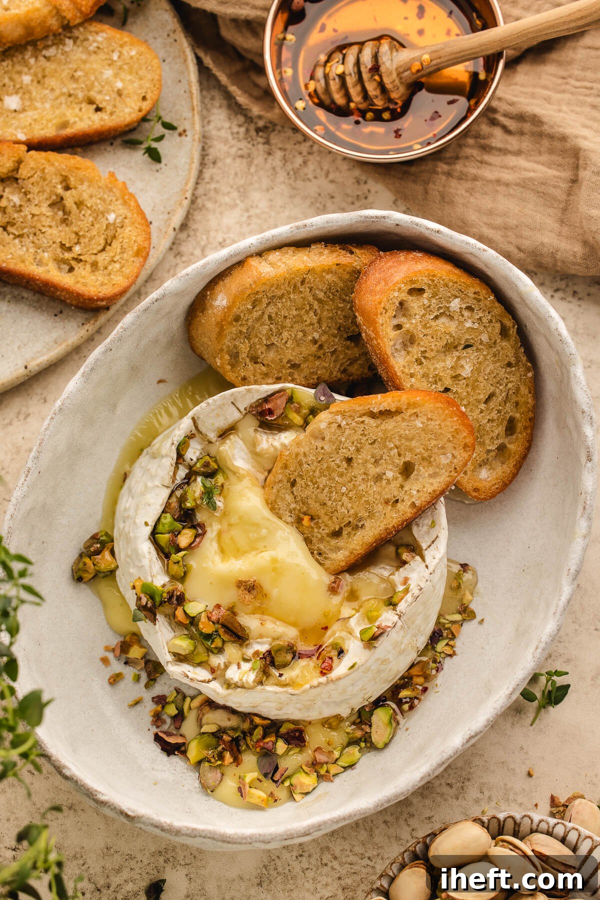 Baked Brie topped with hot honey, chopped pistachios, and thyme, served with toasted crostini for an easy holiday appetizer.
