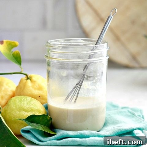 A jar of lemon tahini dressing with a small whisk and lemons in the background. This tahini dressing is ready for a salad.